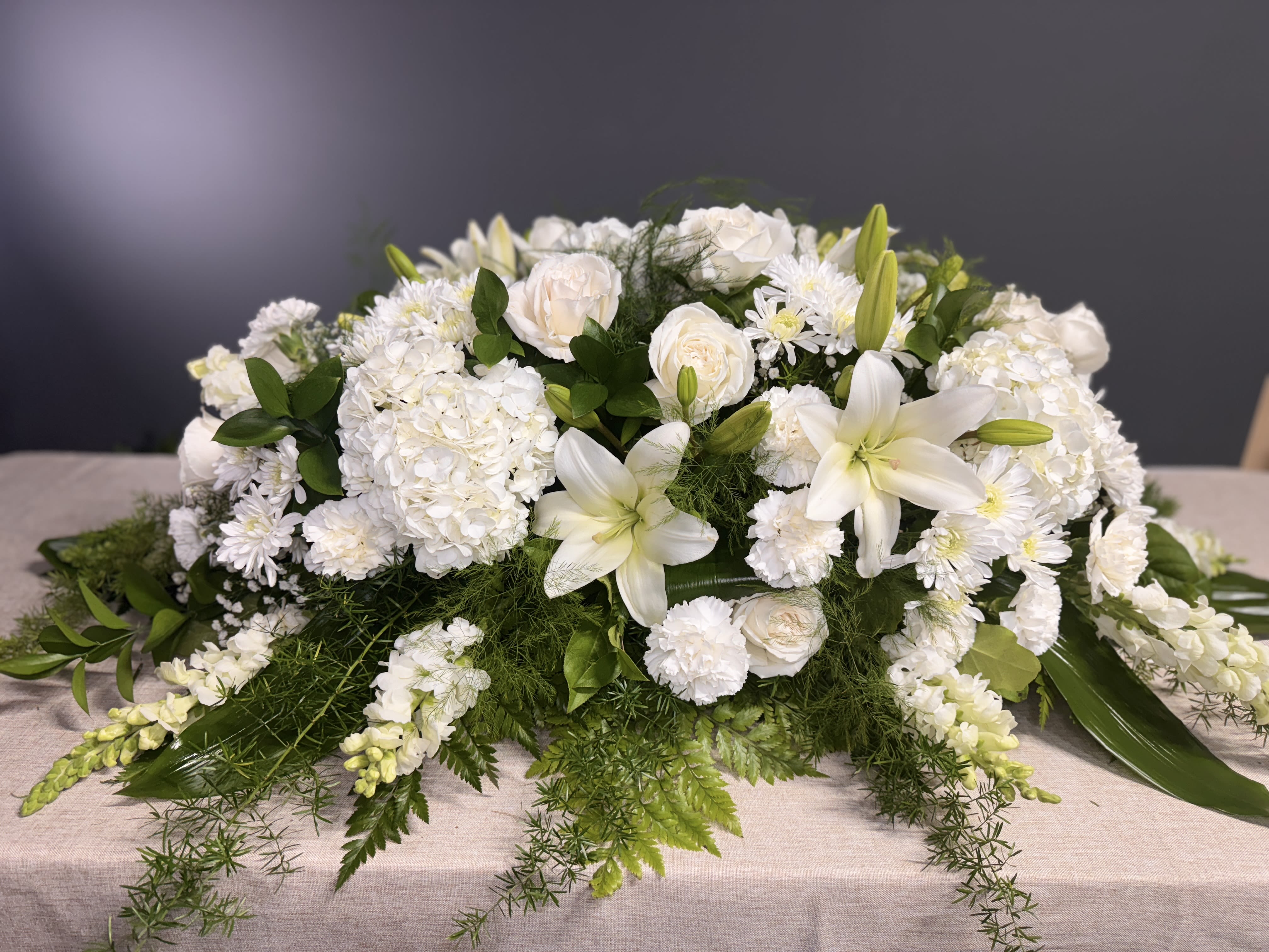 White floral casket spray with lilies, roses, and chrysanthemums
