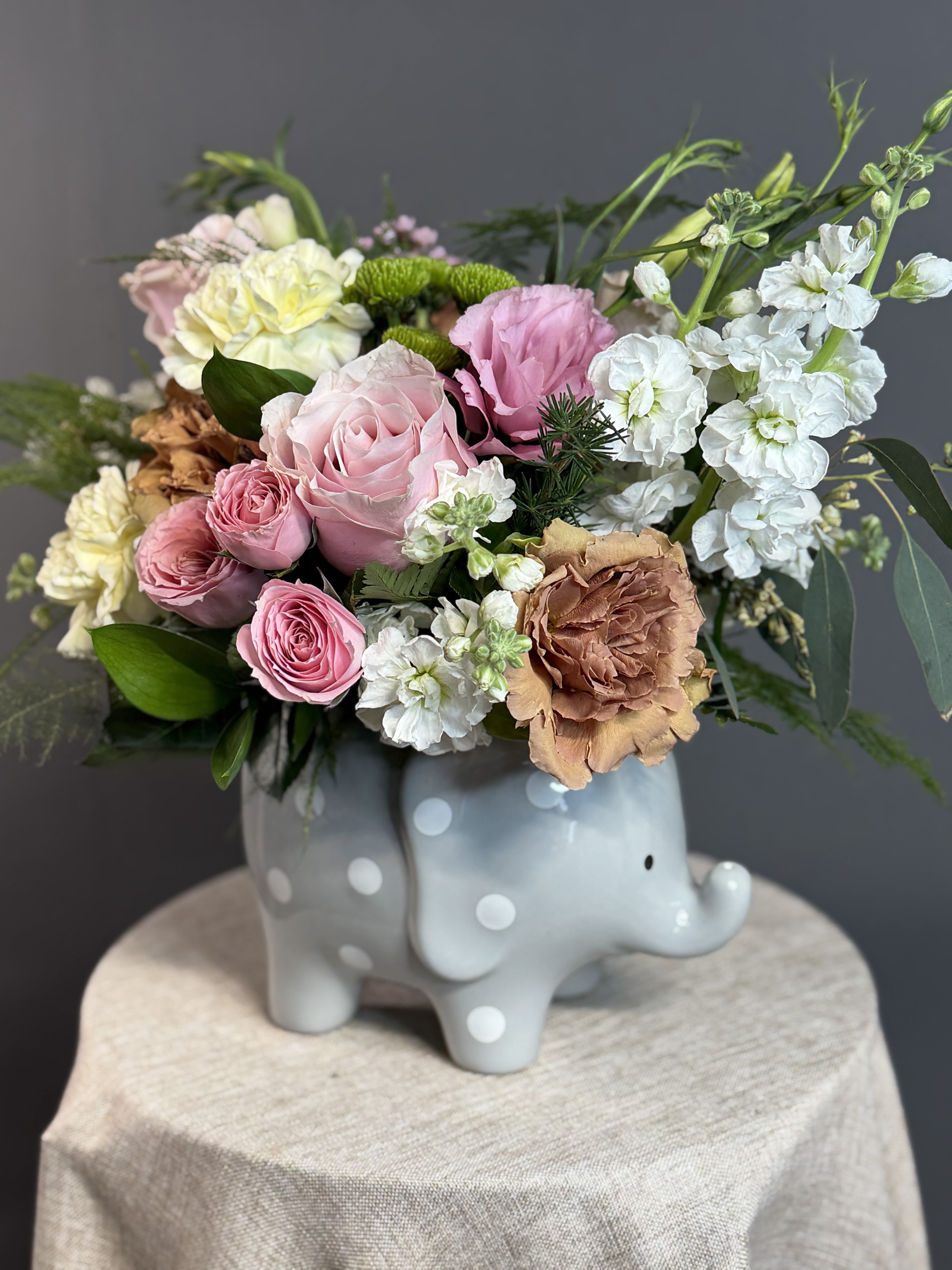 Pink Baby Snuggles Elephant - A sweet and delicate arrangement featuring soft pink blooms, creamy accents, and lush greenery, thoughtfully designed in a charming keepsake elephant vase. Pink Baby Snuggles Elephant is the perfect way to celebrate a precious new arrival with warmth and love 