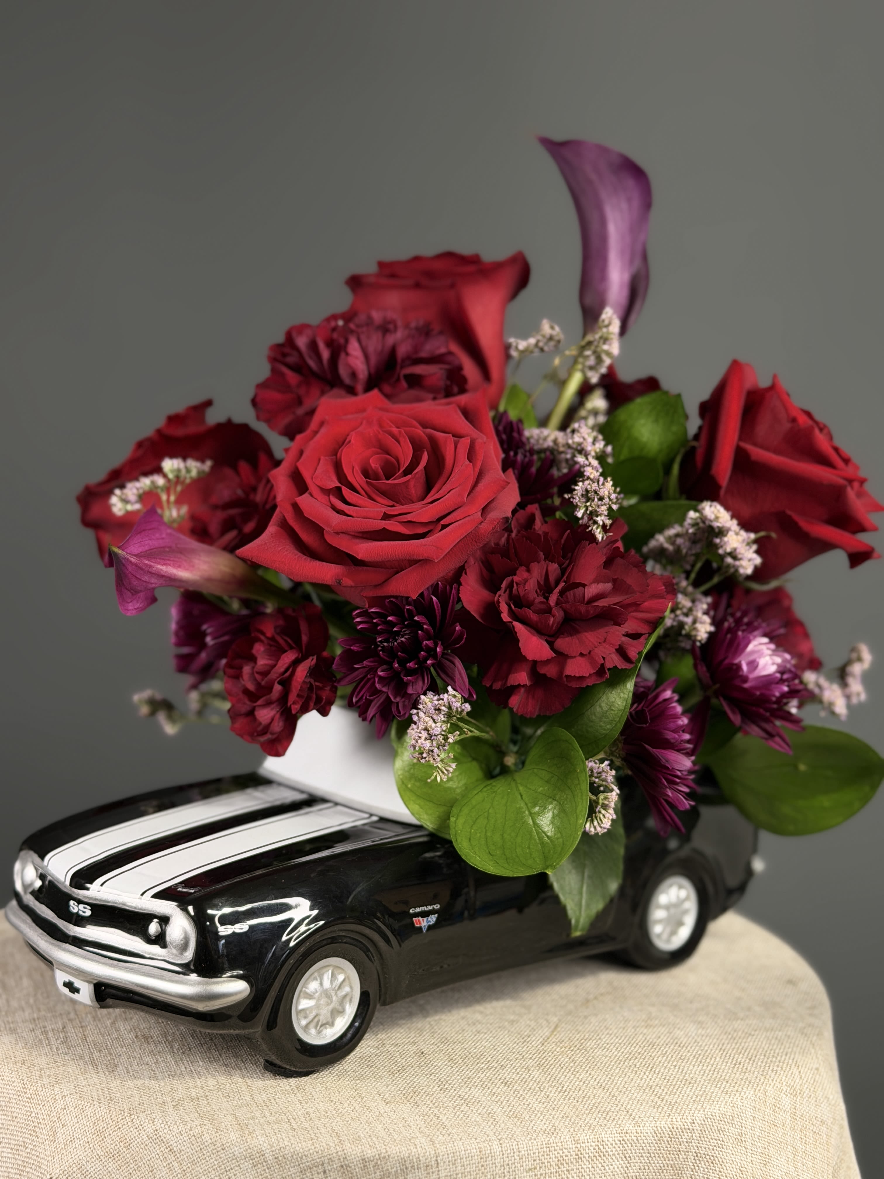 Dark Knight  - Deep, romantic reds and plum tones are tucked into a glossy ceramic Chevy Camaro with white racing stripes for a playful, collectible presentation-perfect as a birthday bouquet, anniversary roses gift, or "just because" surprise that will make the person you're thinking of feel noticed.    Substitutions of flowers may be made when necessary, but we'll preserve the overall color palette and bold, whimsical style.