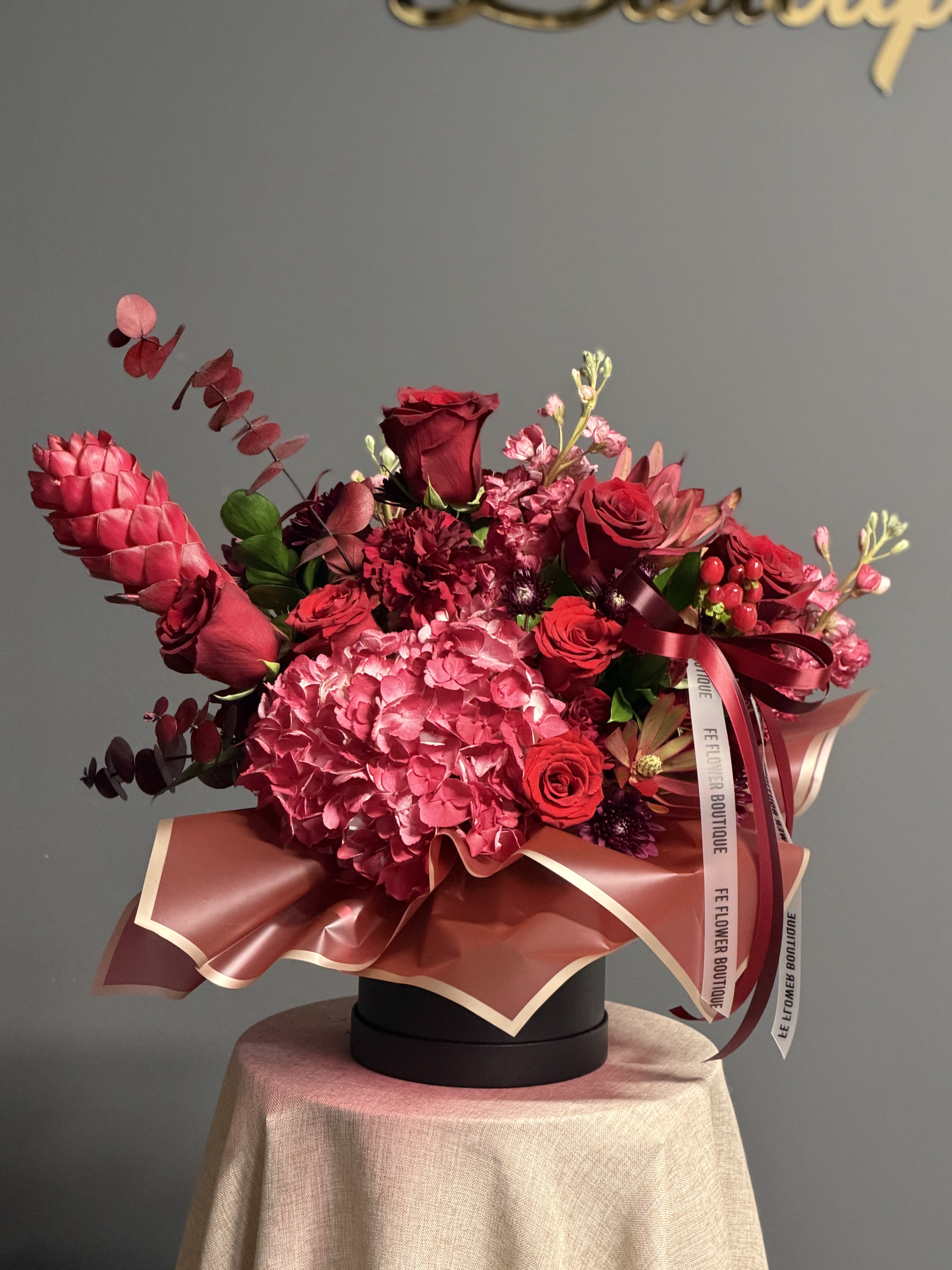 Red and pink floral arrangement in a round black box with ribbon
