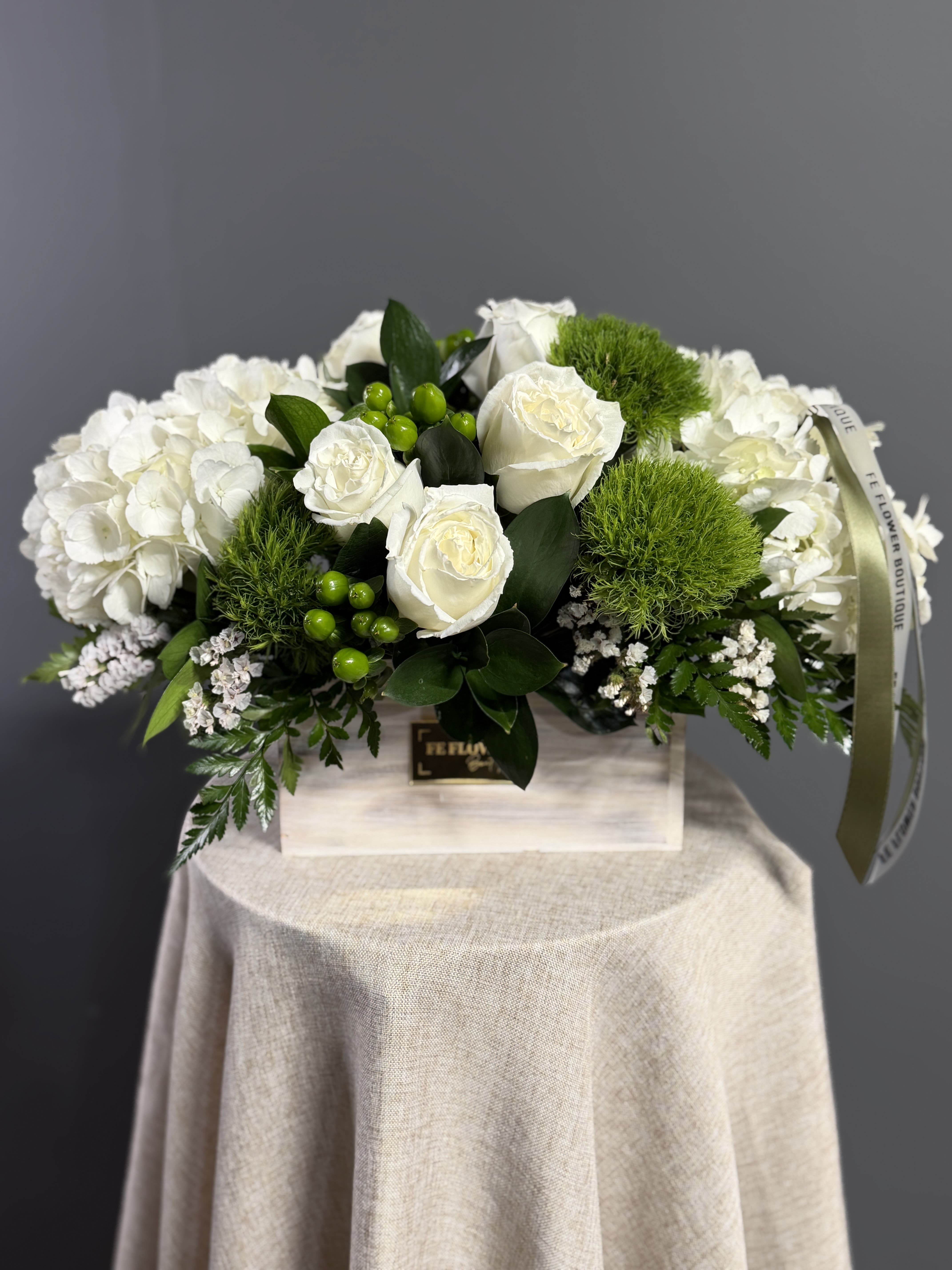 Low white arrangement of roses, hydrangeas, and green dianthus in a rectangular wooden box.
