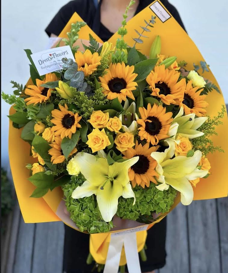 Bouquet of yellow sunflowers, roses, and lilies wrapped in bright orange paper