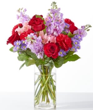 Bouquet of red roses and purple flowers in a clear glass vase