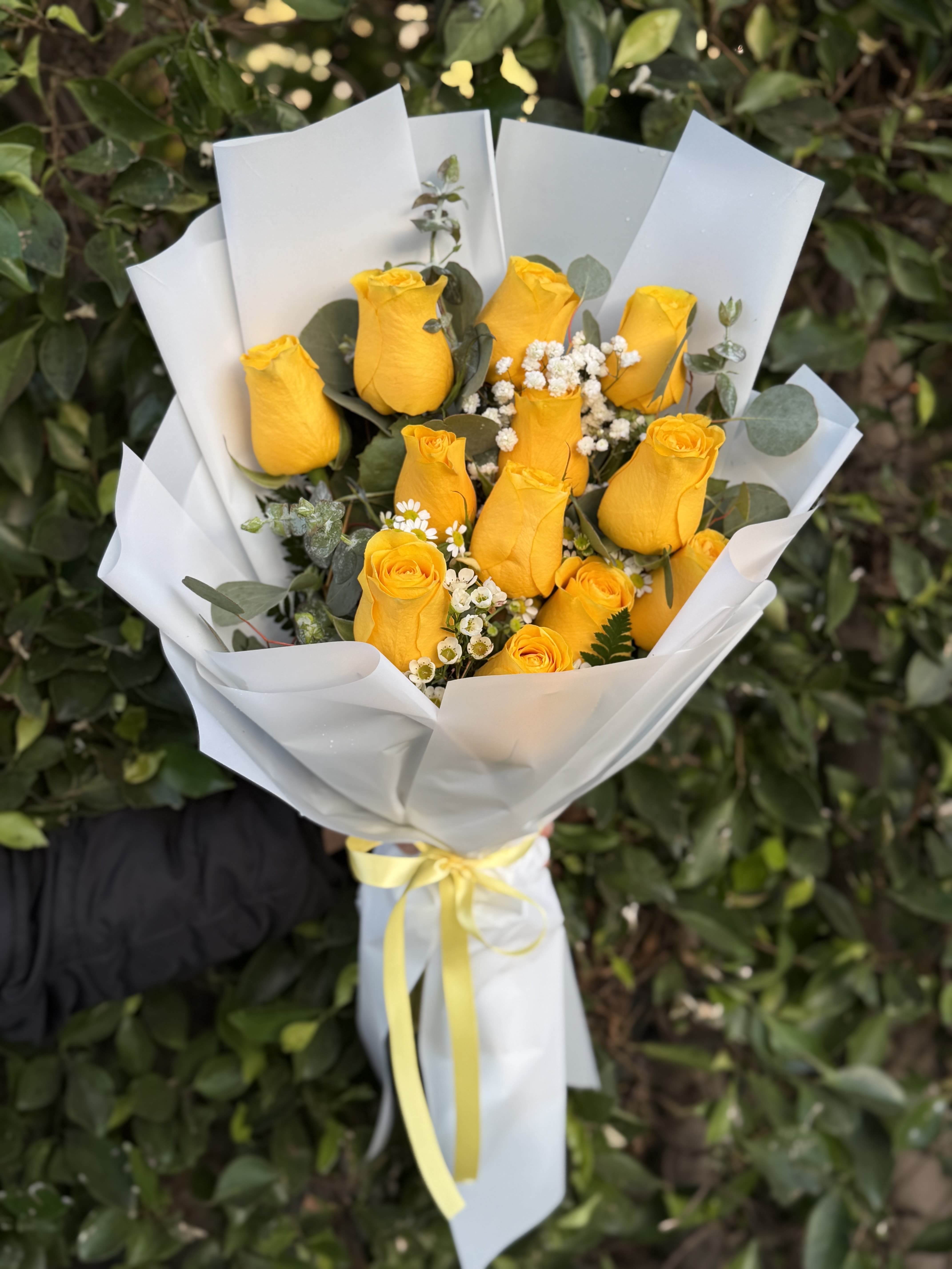 Golden Glow- 12 - Bright, happy, and full of charm—this wrapped handheld bouquet features 12 vibrant yellow roses accented with airy textures and fresh greens. Designed to feel light and uplifting, it’s the perfect way to share joy, appreciation, or a simple “thinking of you.”