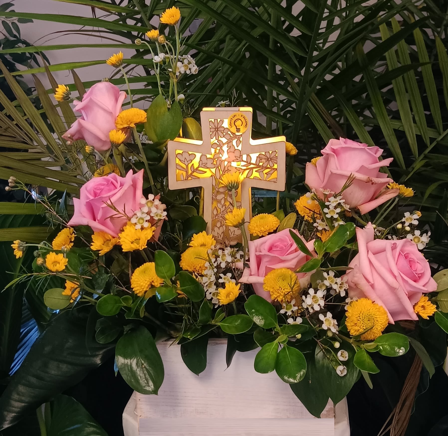 Pink roses and yellow flowers arranged around a lit decorative cross