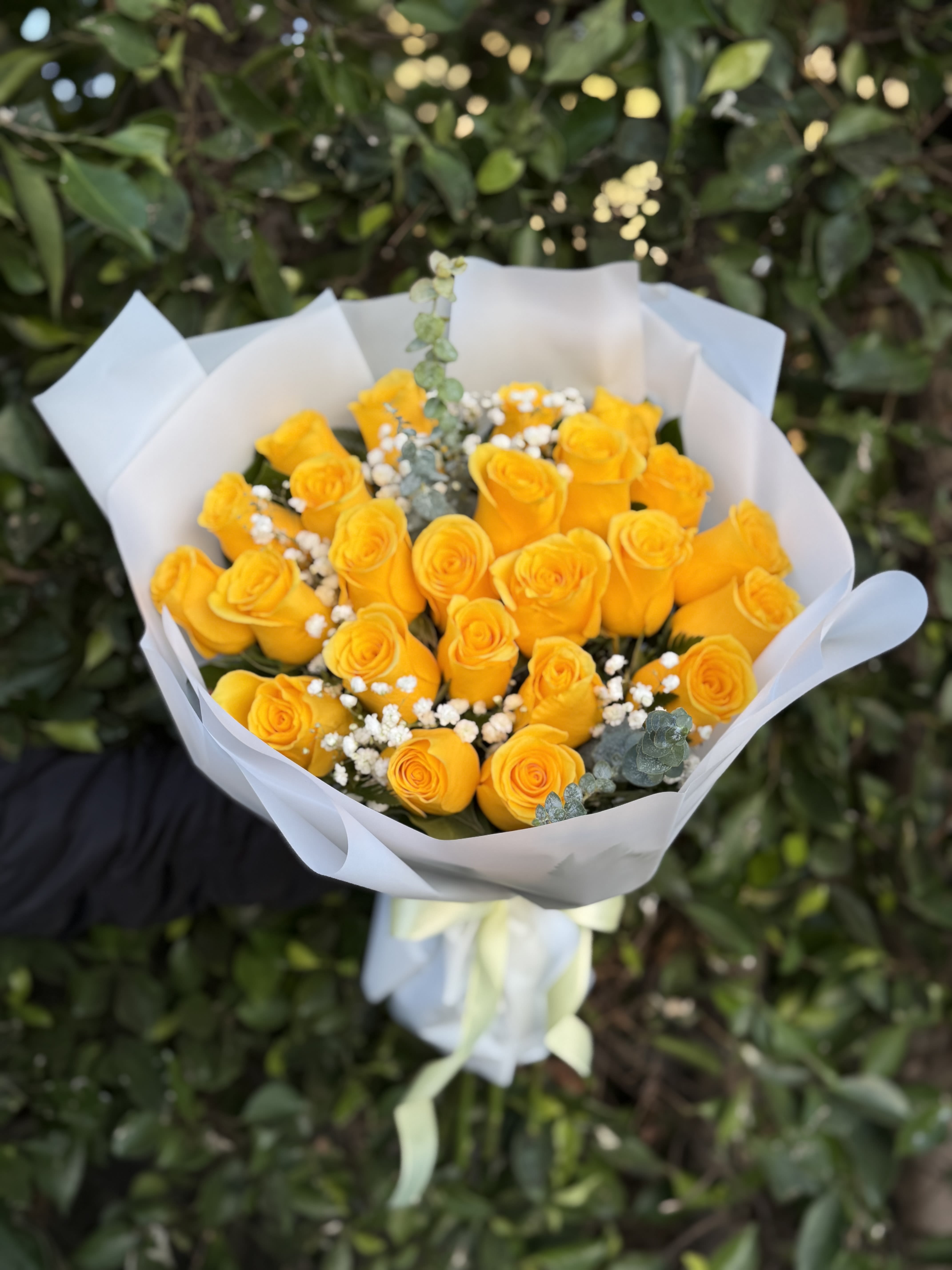 Golden Glow-24 - Bright, happy, and full of charm—this wrapped handheld bouquet features 24 vibrant yellow roses accented with airy textures and fresh greens. Designed to feel light and uplifting, it’s the perfect way to share joy, appreciation, or a simple “thinking of you.”