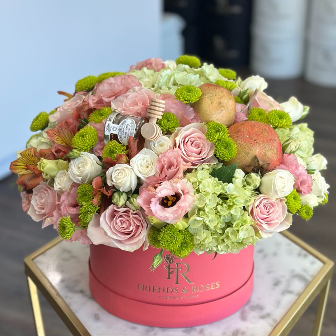 Pink and white roses with green pompons in a round pink box