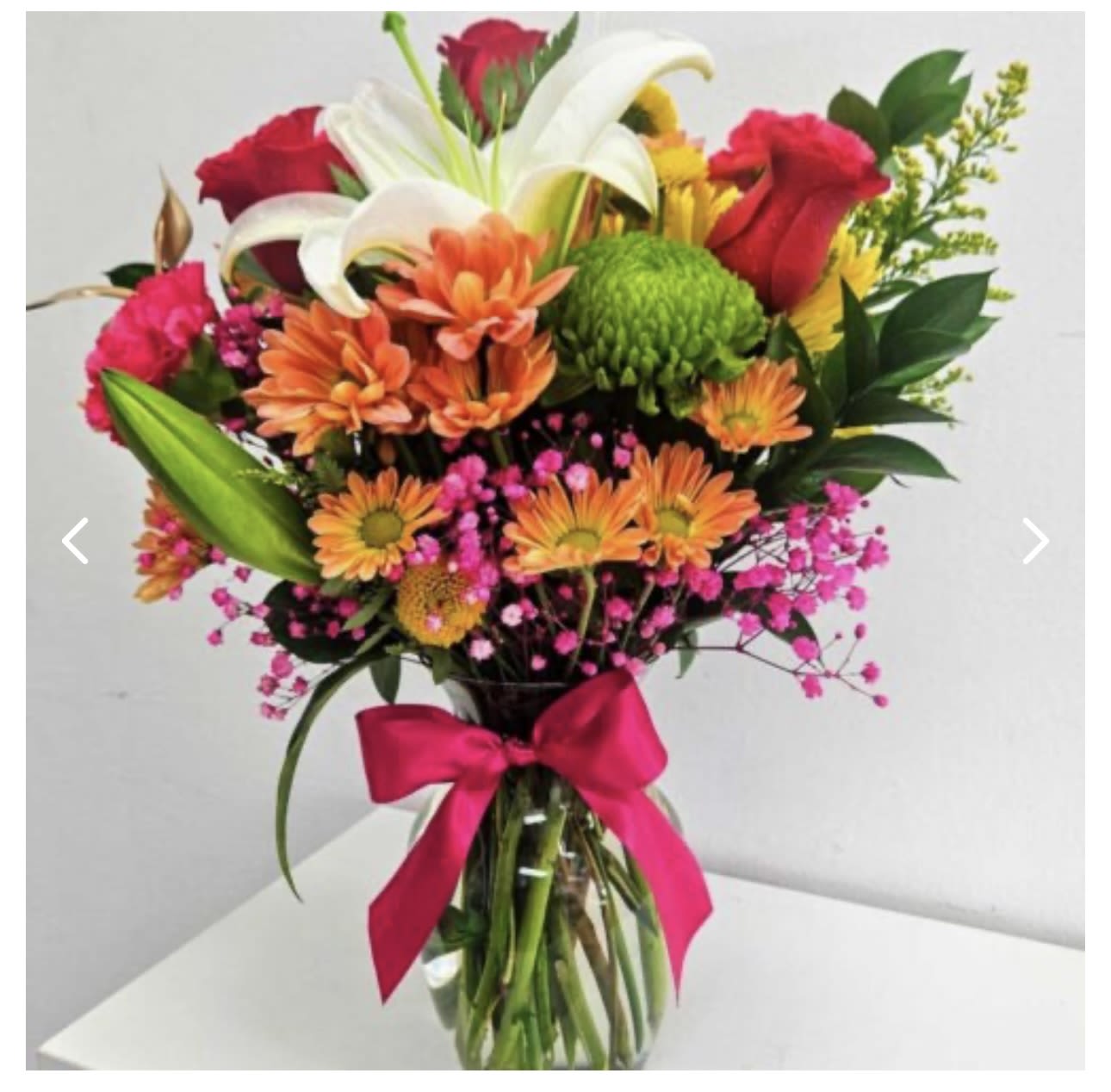Mixed bouquet of lilies, roses, and daisies in a glass vase with a pink ribbon