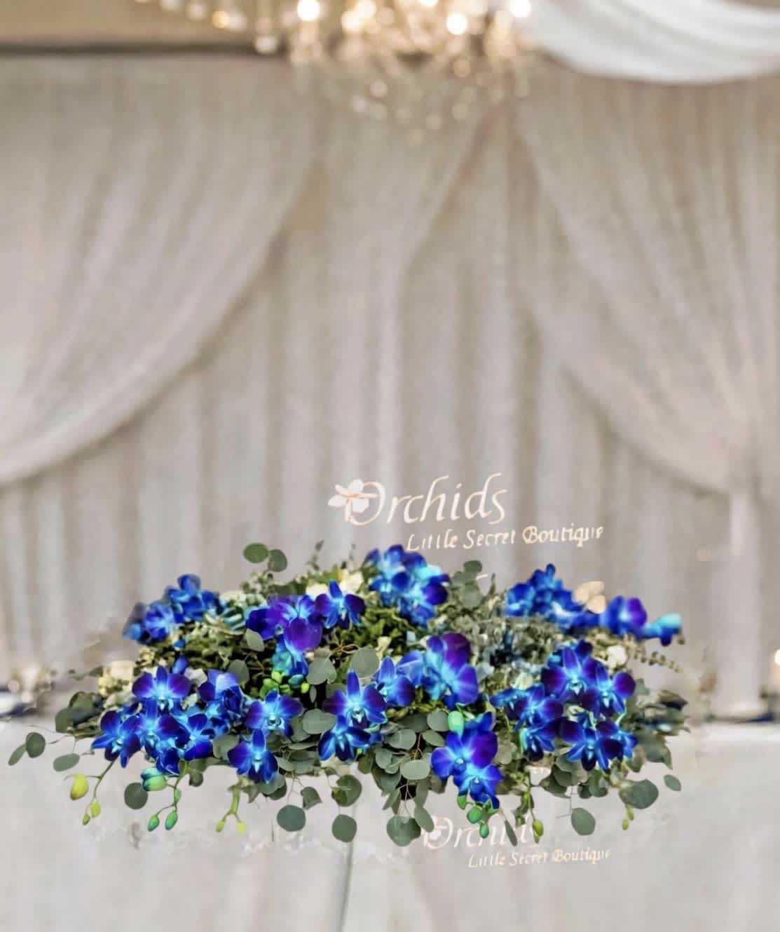 Low floral arrangement with vivid blue orchids and greenery on a wedding table