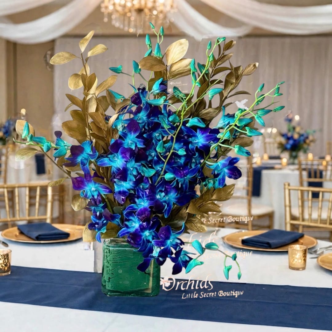 Blue orchid centerpiece in a green glass vase with gold foliage