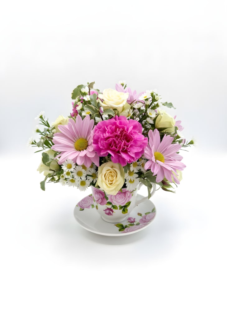 Tea Party Bouquet - Sweet, delicate, and full of storybook charm, this petite arrangement brings a touch of whimsy to any moment. Lavender daisies, creamy white roses, and dainty white blooms gather around a vibrant pink carnation, creating a fresh‑from‑the‑garden look that feels both nostalgic and uplifting. Nestled inside a vintage‑style floral teacup and saucer, it’s a keepsake piece that delights long after the flowers fade.