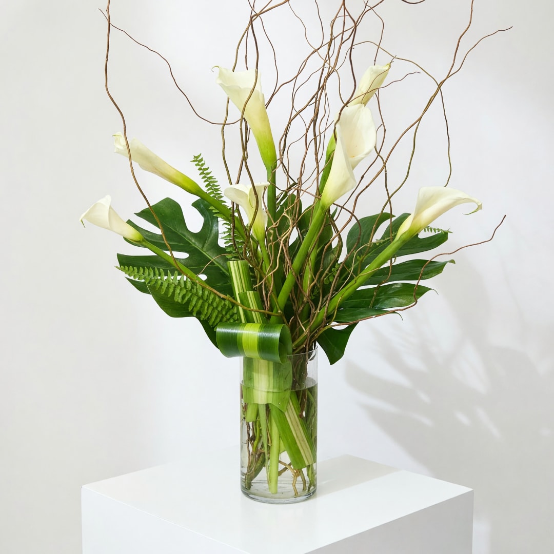 White calla lilies in a clear glass vase with curly branches