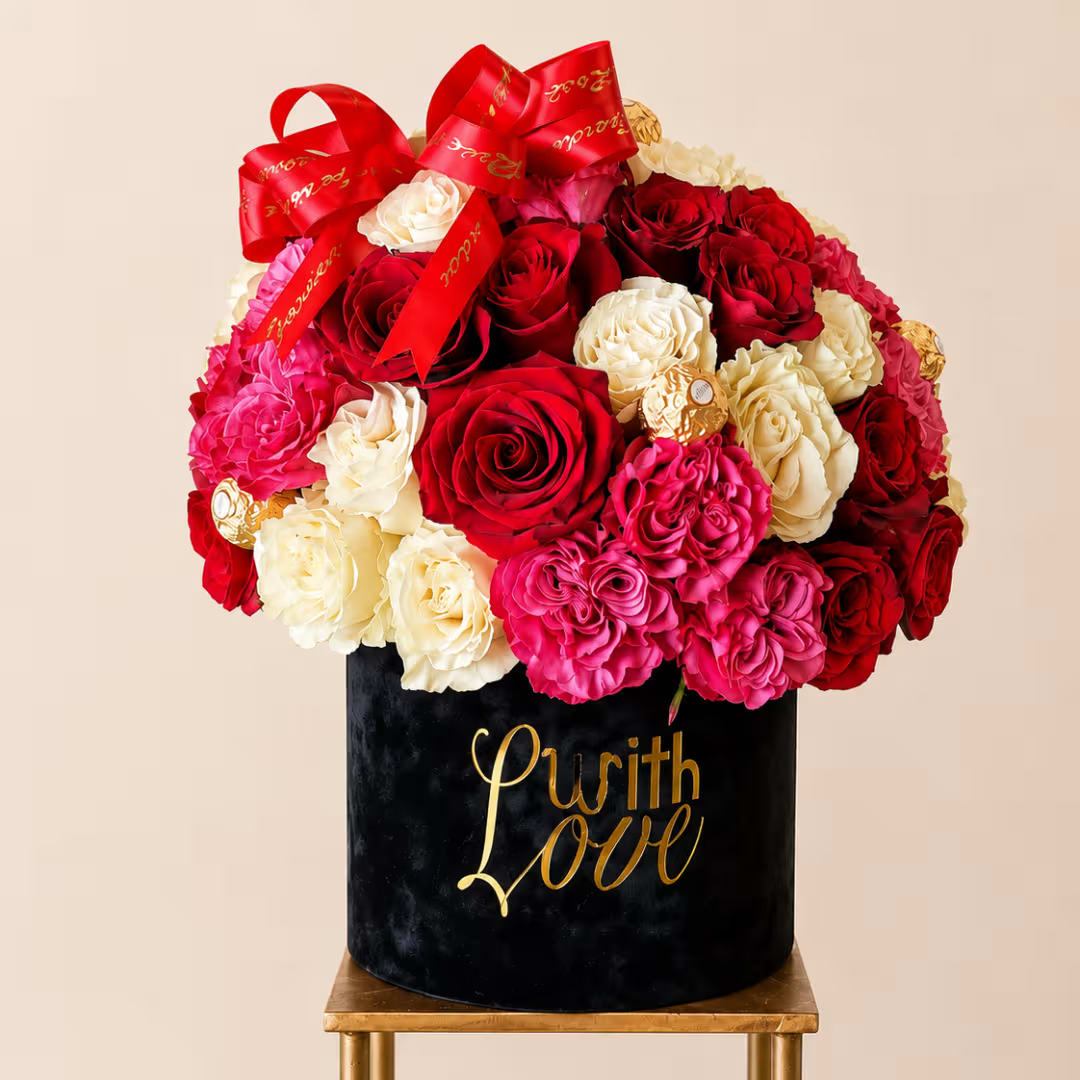 Red, pink, and cream roses arranged in a black box with red ribbons