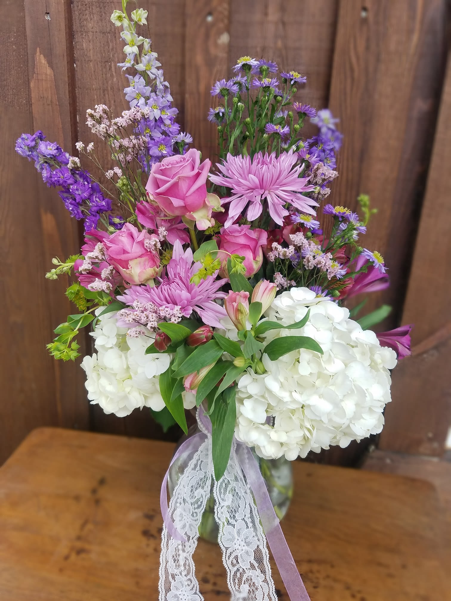 Pink roses and purple flowers arranged in a glass vase with white hydrangeas
