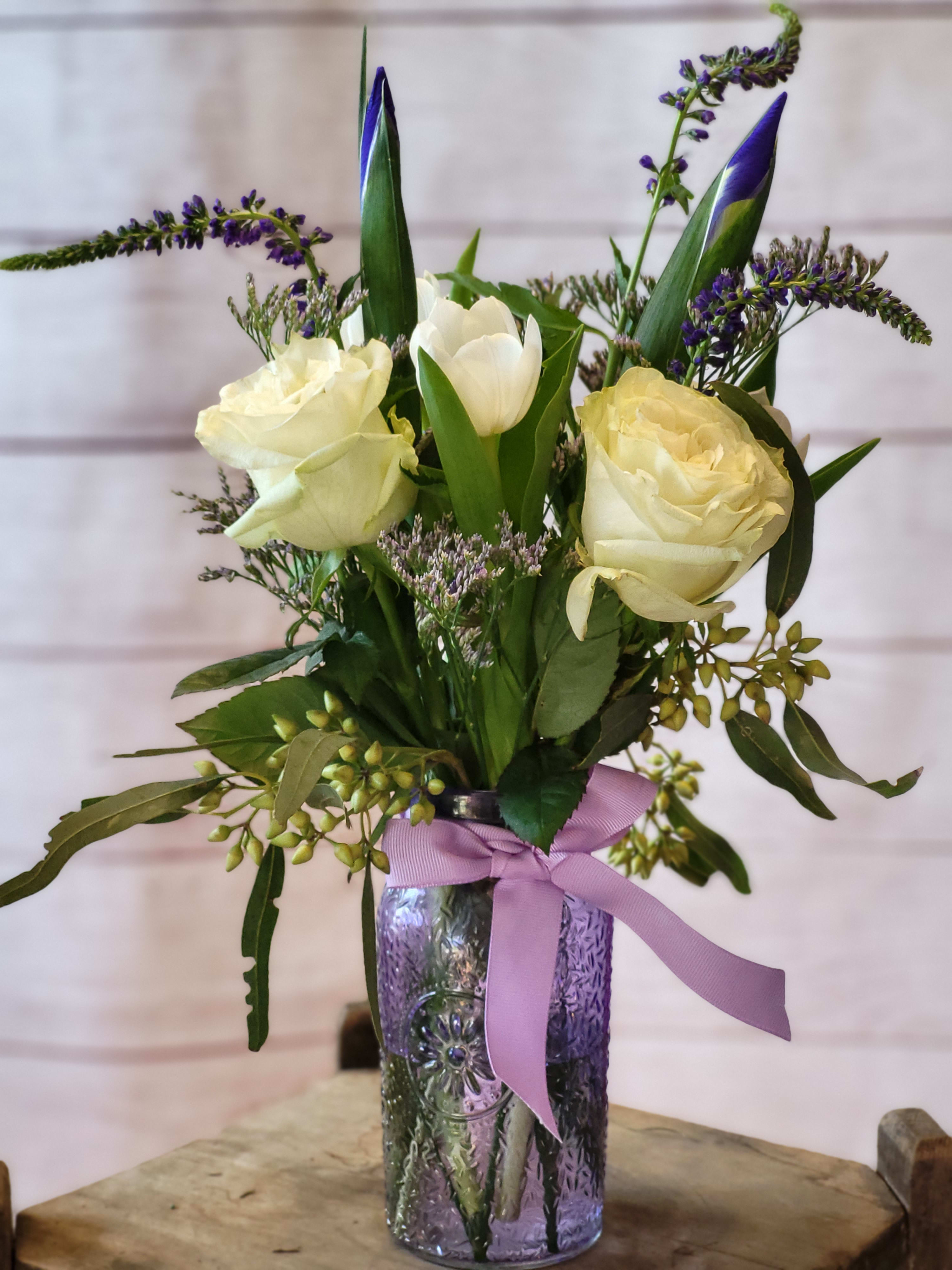 White roses and tulips in a purple glass vase with a lavender ribbon