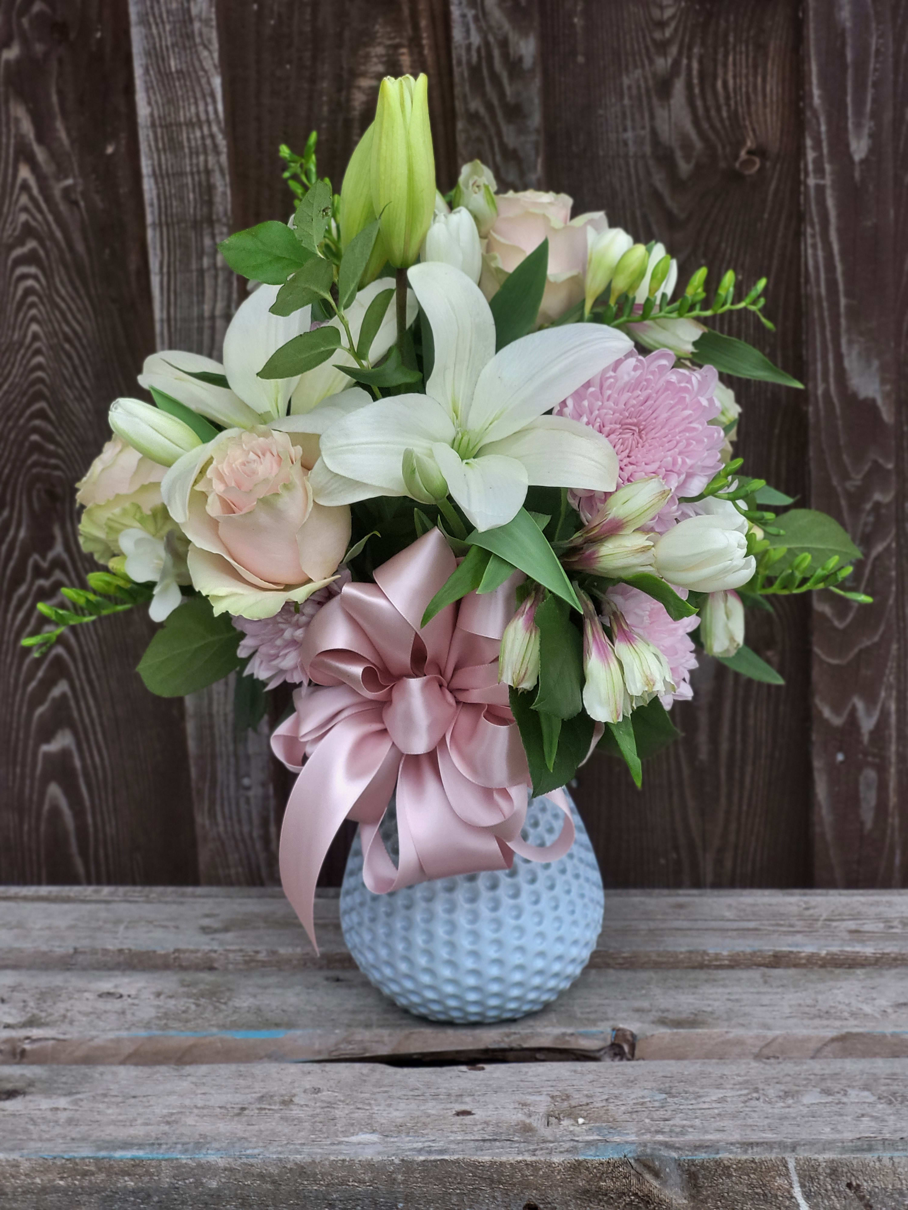 Bouquet of white lilies and pale pink roses in a blue vase with a pink ribbon