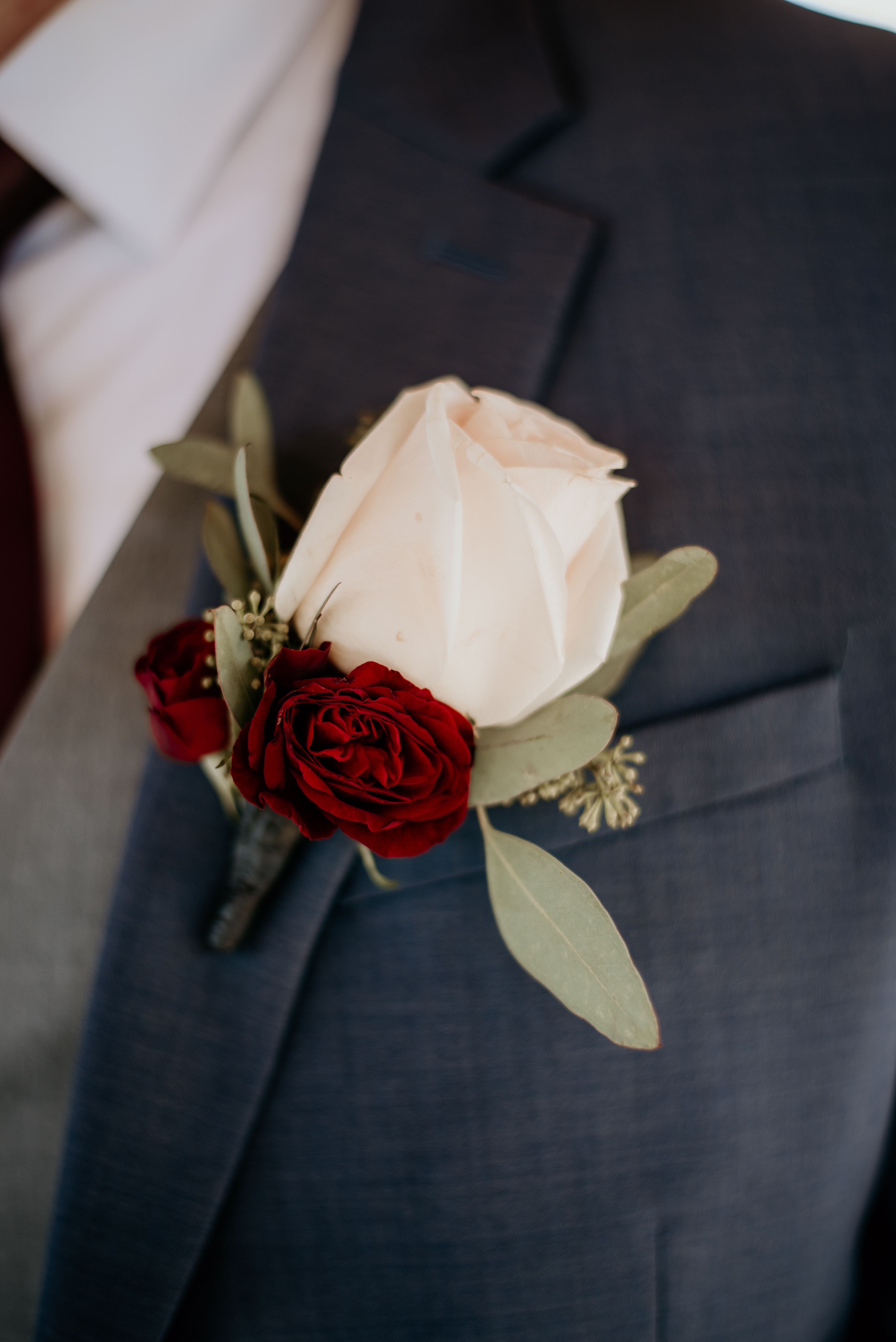 White rose boutonniere with red roses on a suit lapel