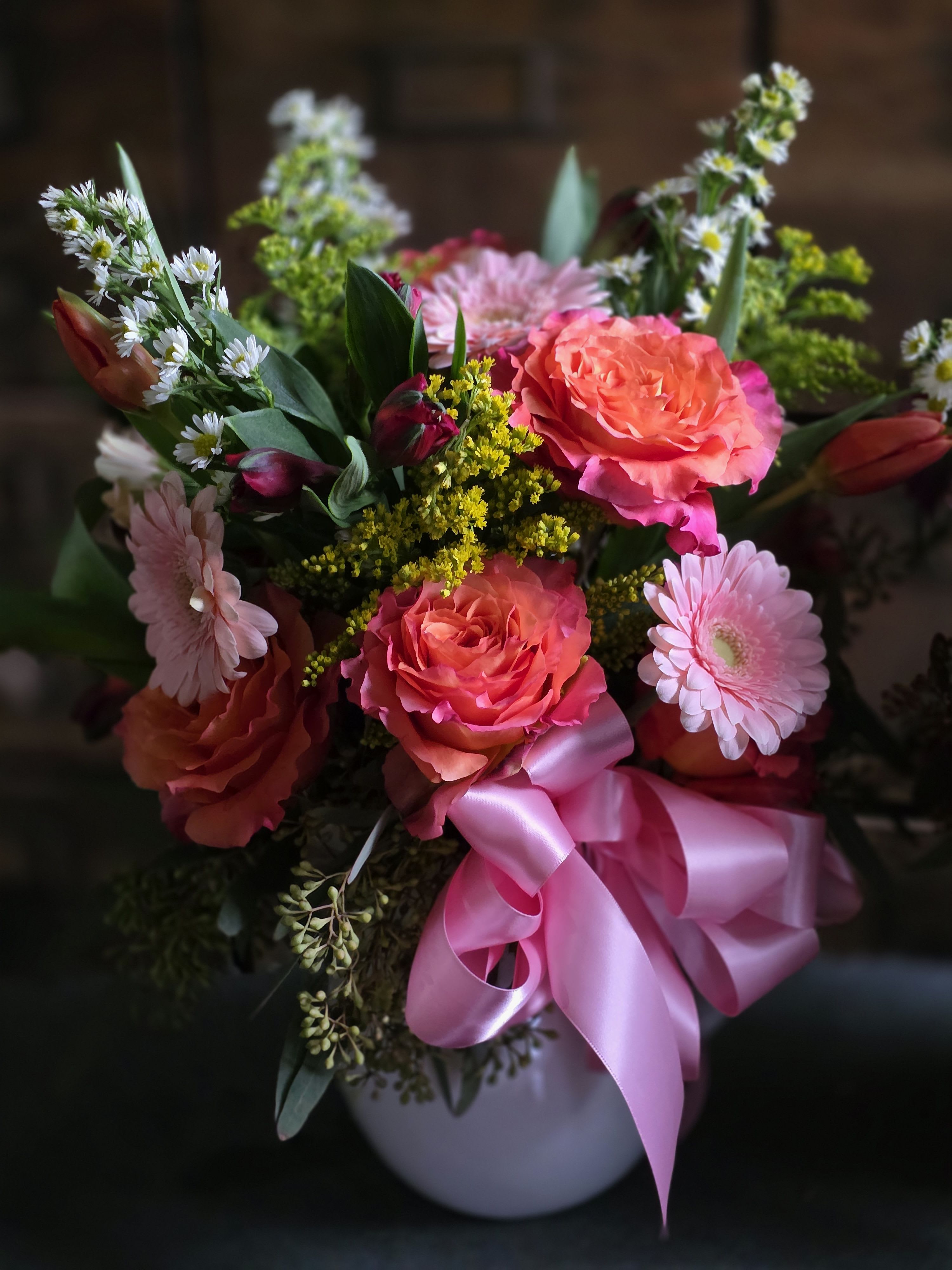 Pink and coral roses with daisies in a white vase, tied with a pink ribbon