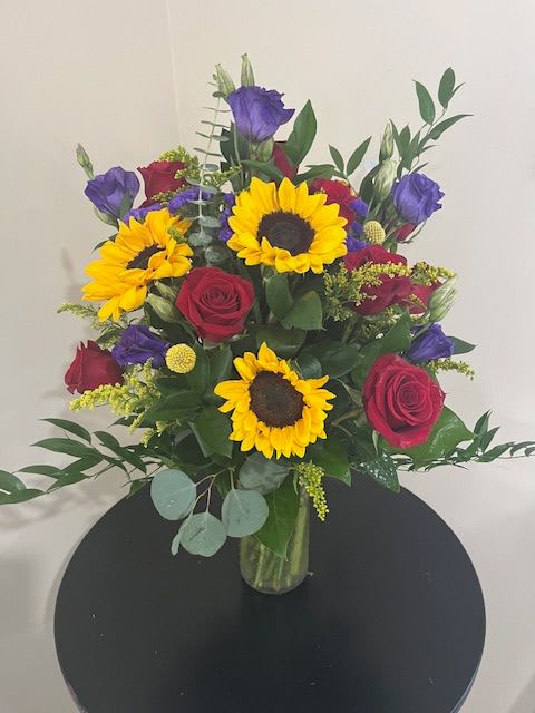Bouquet of sunflowers, red roses, and purple blooms in a glass vase