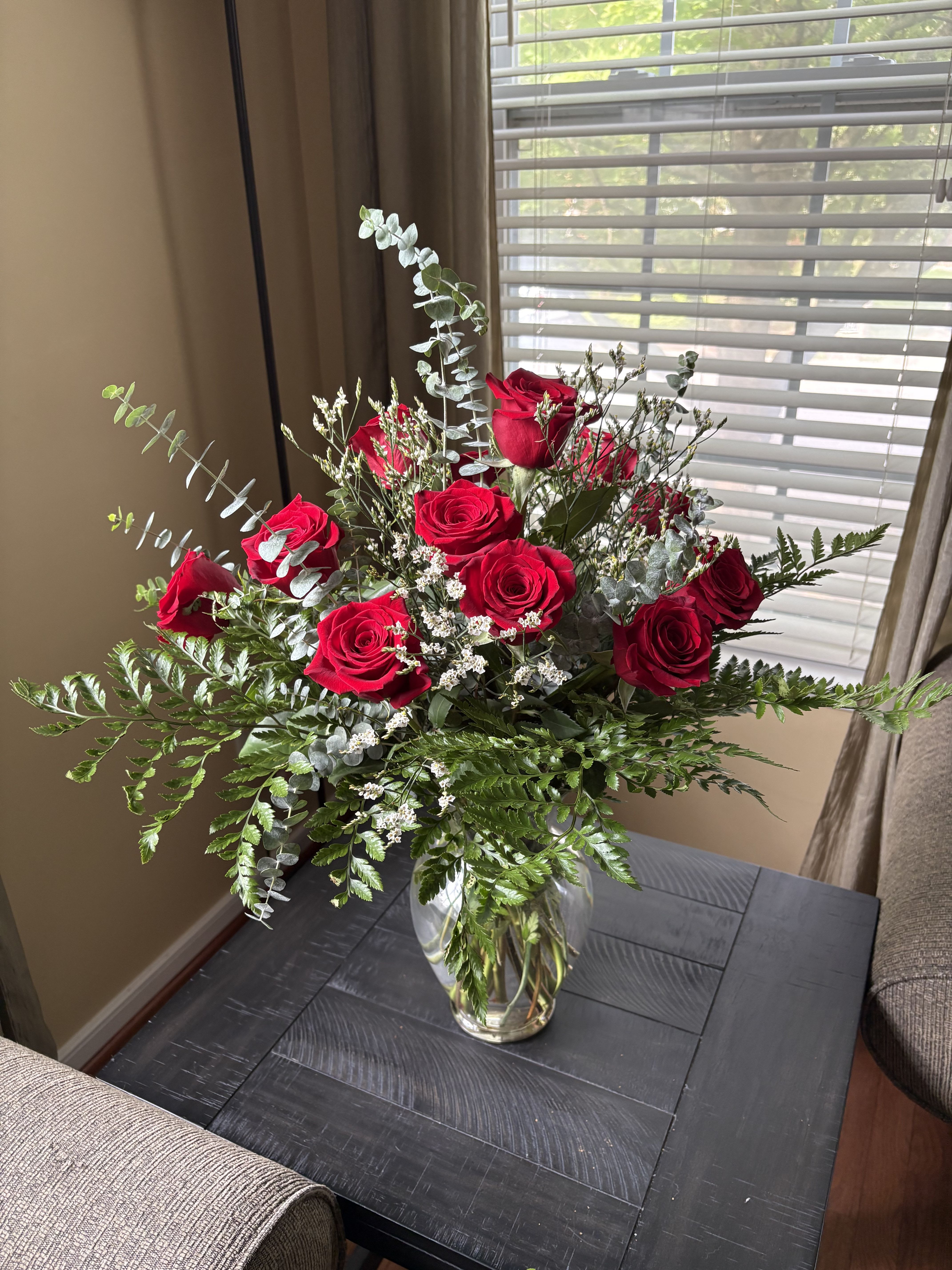 Red roses arranged in a clear glass vase with airy greenery