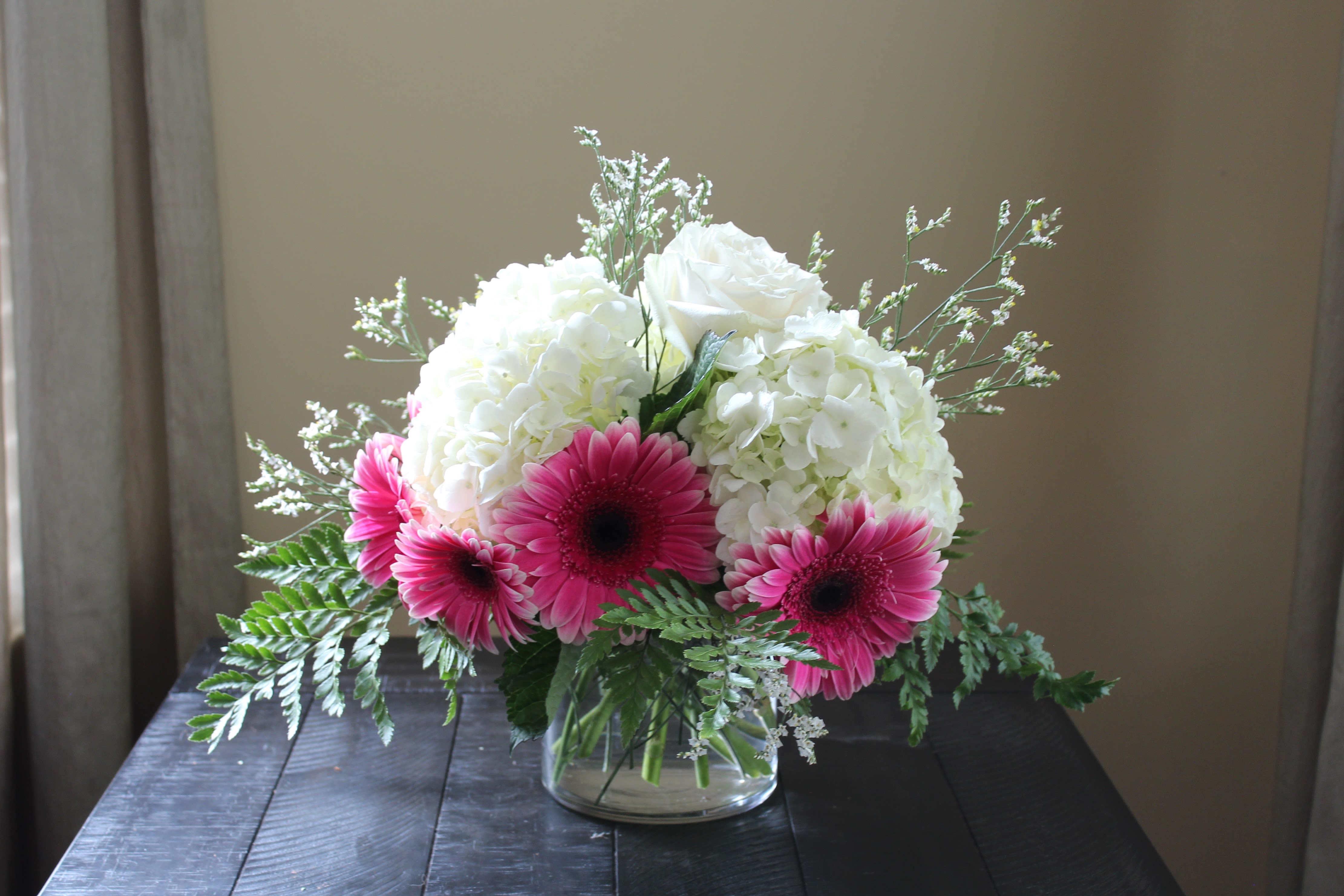 Pink gerbera daisies and white hydrangeas in a clear glass vase