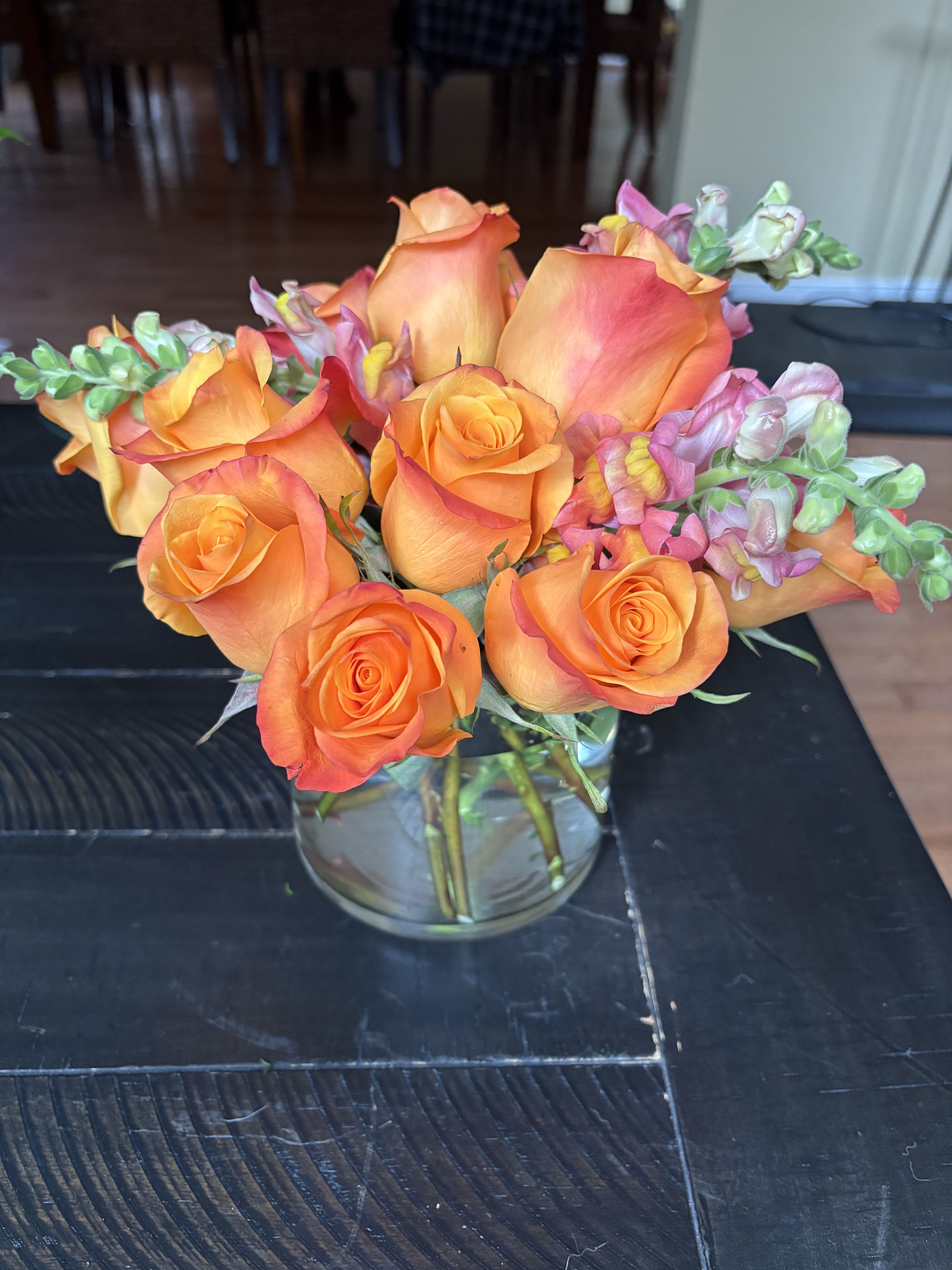 Orange roses and pink snapdragons arranged in a clear glass vase