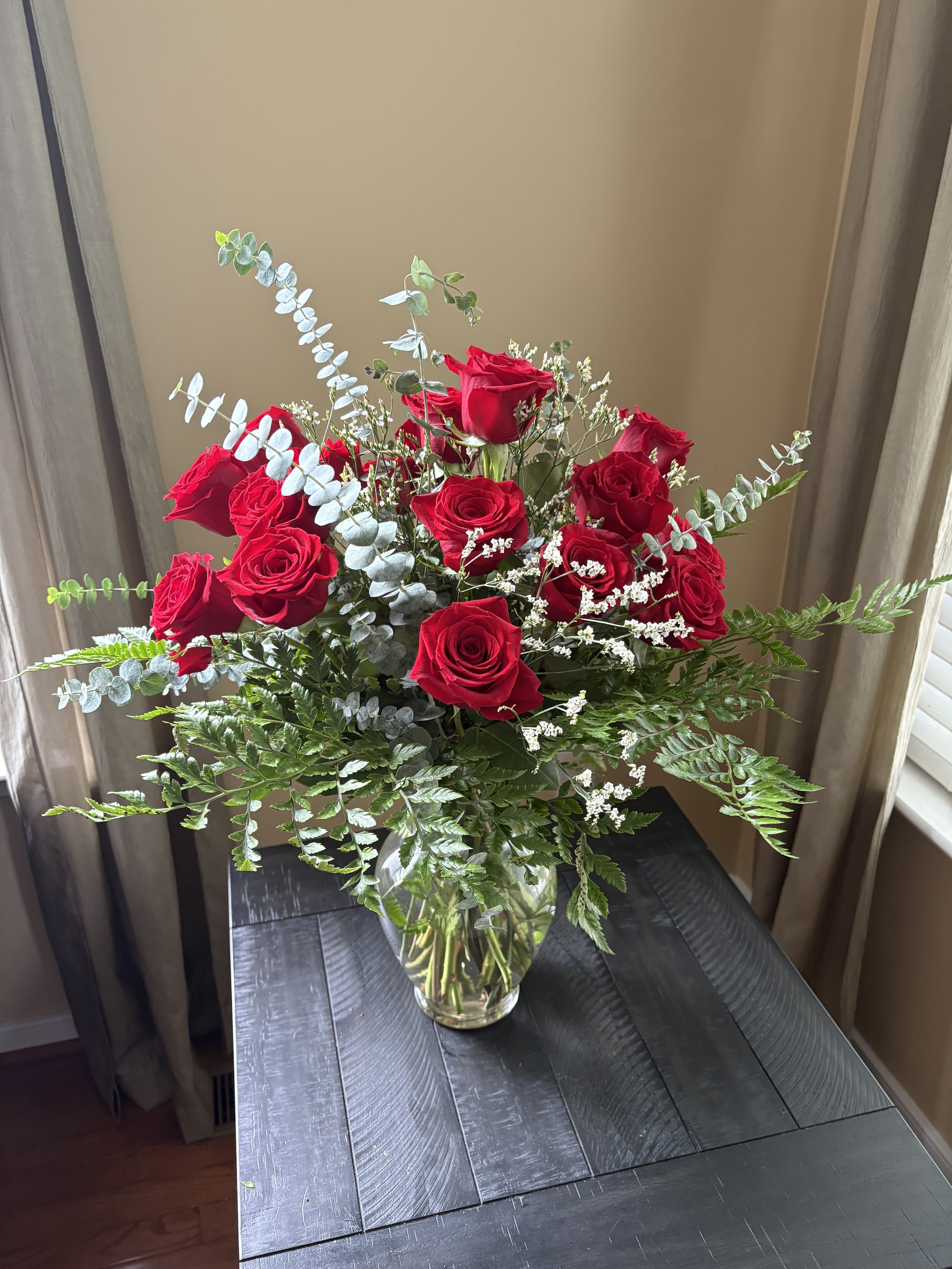 Modern Romance - 18 Red Roses w/ Premium Filler - Make a timeless statement of love and elegance with our 18 Red Roses with Premium Filler arrangement. Each luxurious red rose is carefully hand-selected for its vibrant color, lush petals, and long-lasting beauty. Complemented by fresh eucalyptus and seasonal premium greenery, this bouquet exudes sophistication and natural charm.  Presented in a sleek, clear glass vase, this arrangement is perfect for anniversaries, romantic gestures, or simply saying “I love you.” The subtle fragrance of eucalyptus adds a modern, refreshing touch that enhances the classic beauty of red roses.  Includes: 18 premium long-stem red roses Elegant eucalyptus and seasonal greenery Clear glass vase Expertly arranged and ready for display  Whether you’re celebrating love, admiration, or appreciation, this stunning floral design delivers a message straight from the heart.