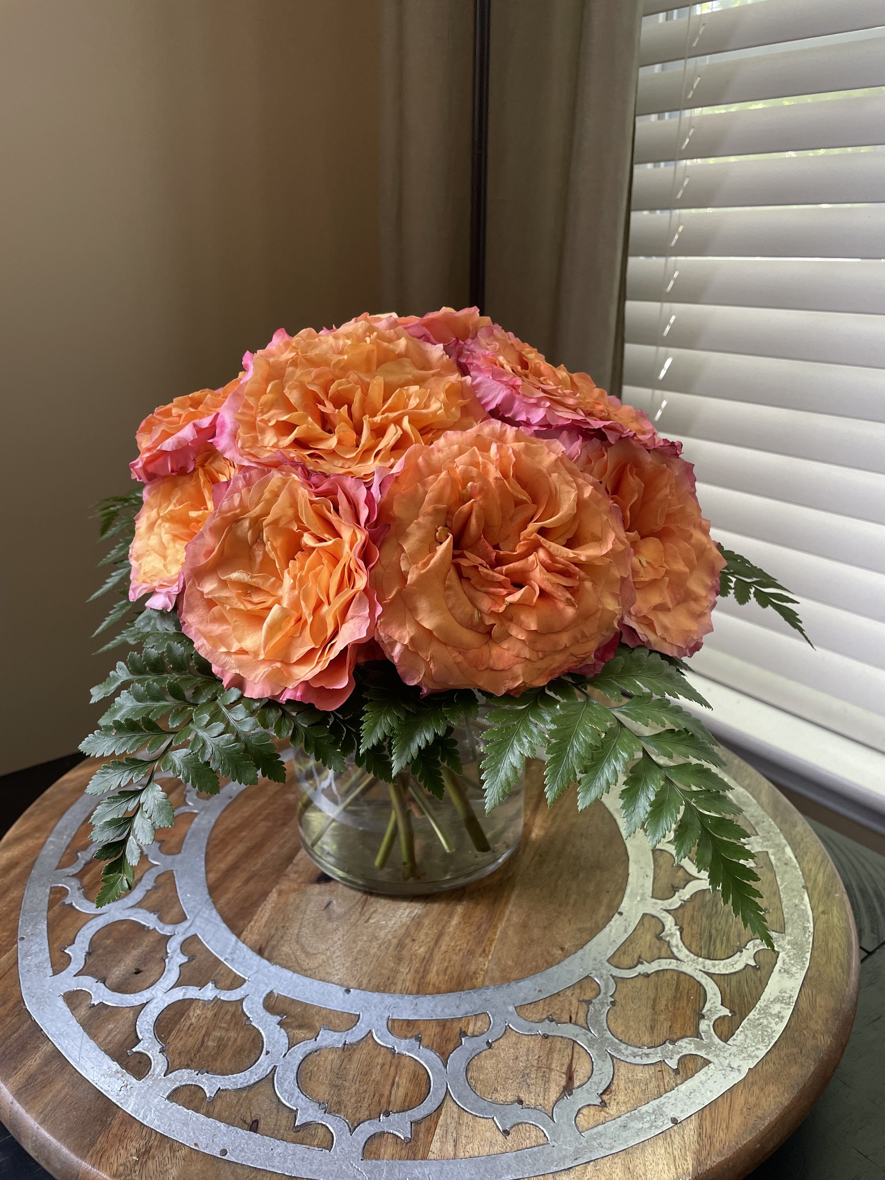 Orange and pink roses in a clear glass vase with fern foliage