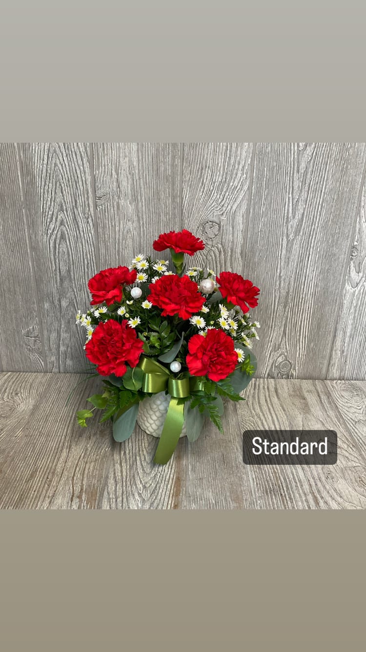 Red carnations with small white daisies in a white vase with a green ribbon