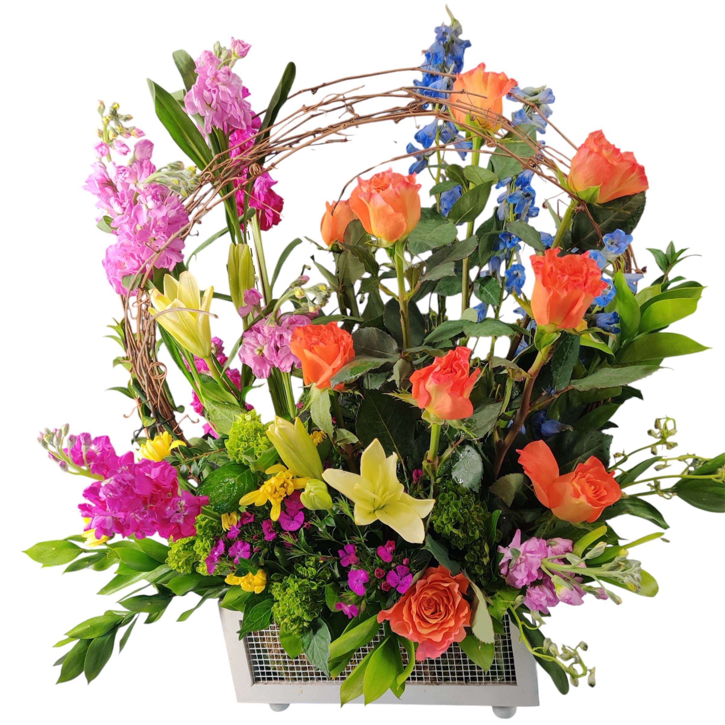 Tall mixed arrangement of orange roses, yellow lilies, and bright blooms in a white rectangular container