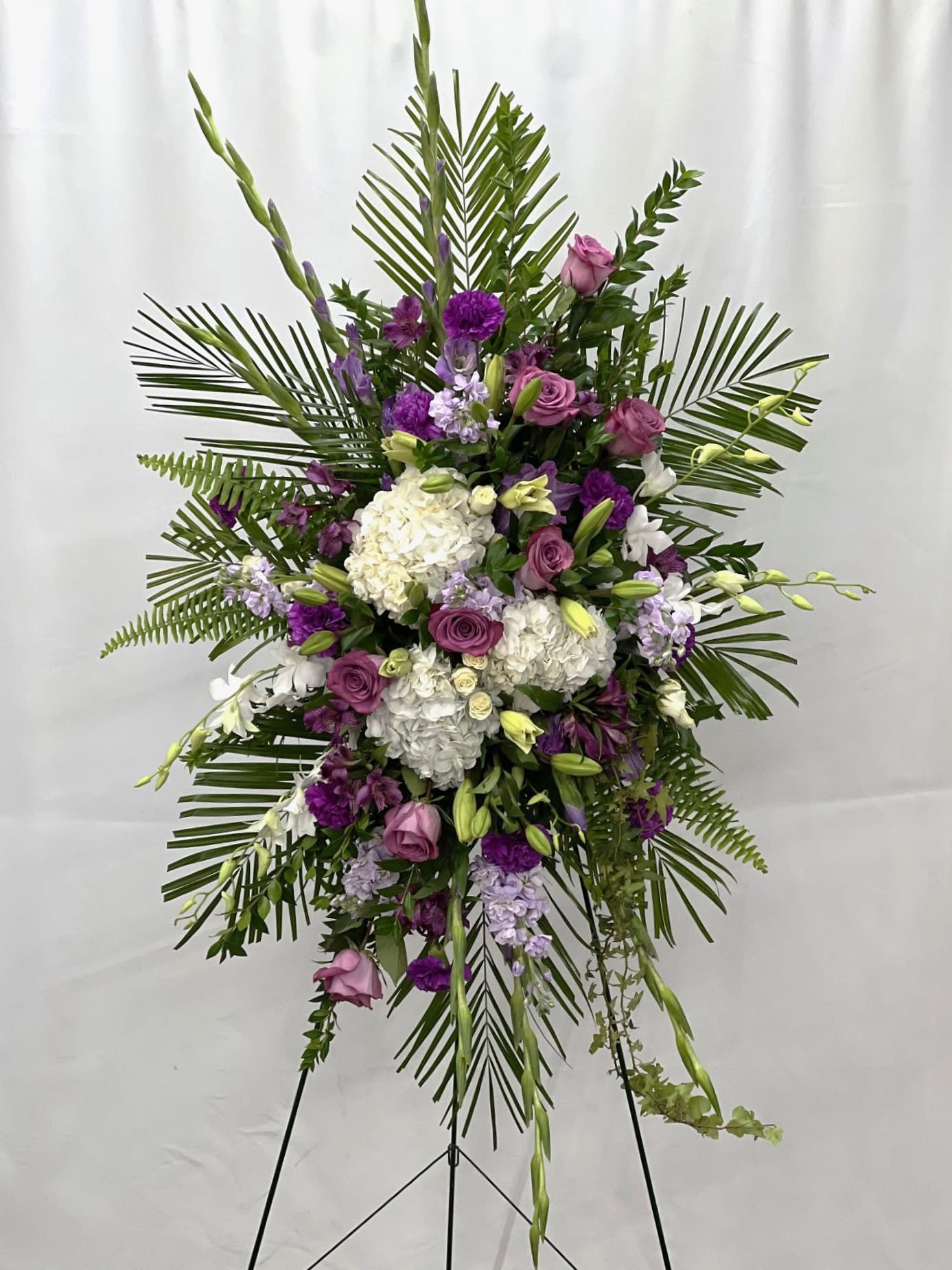 Standing floral spray with purple and white flowers on a tripod easel