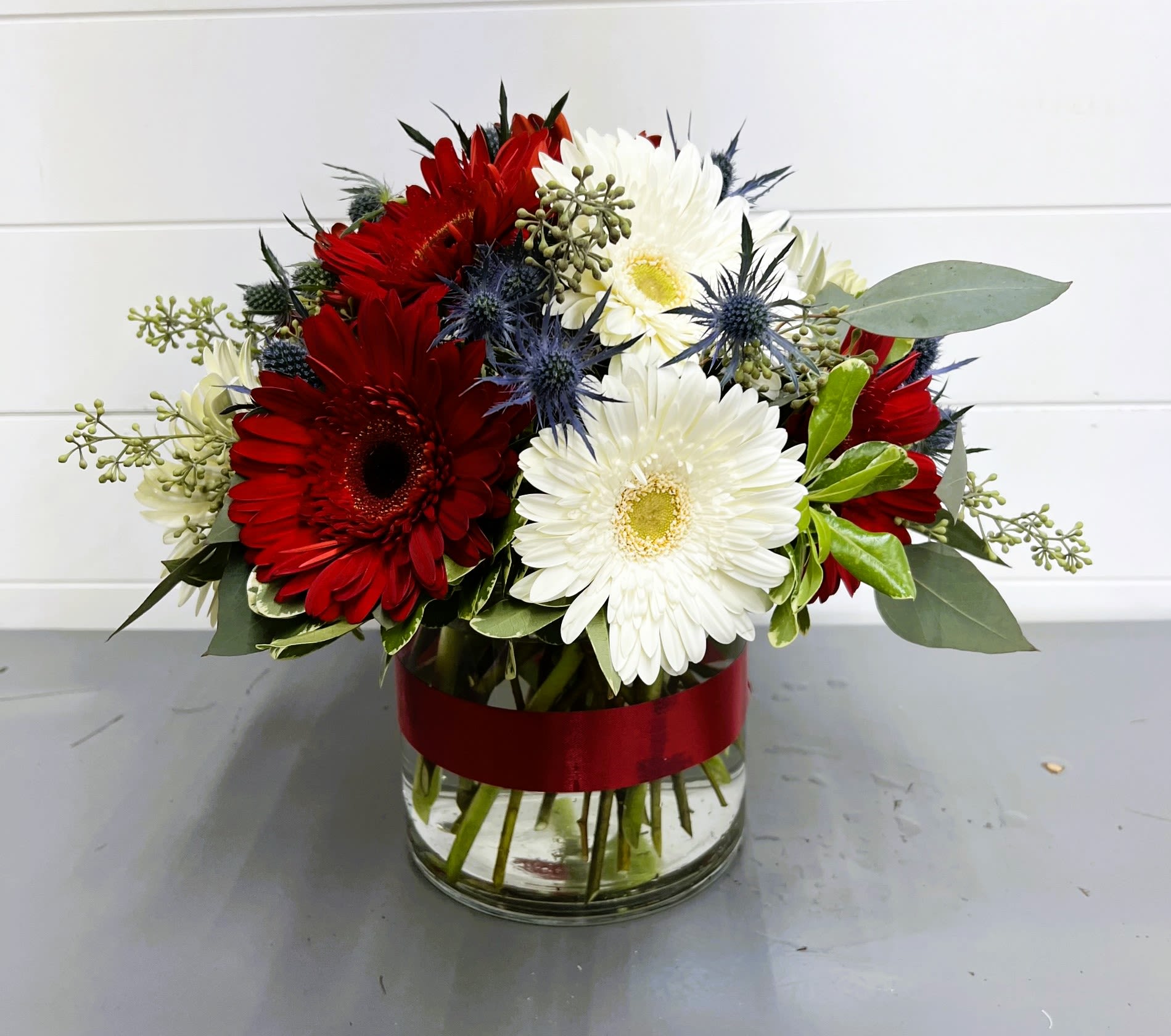 Red and white gerbera daisies in a glass vase with a red ribbon