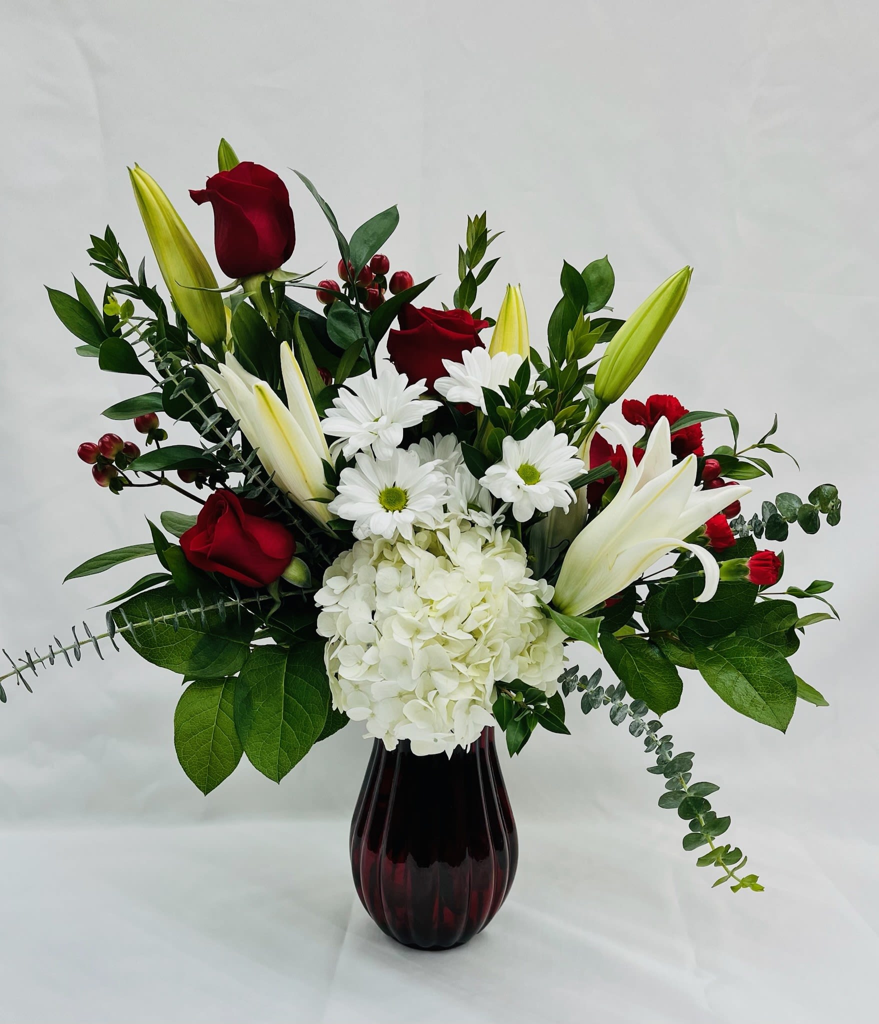 Red roses and white lilies with daisies in a dark vase