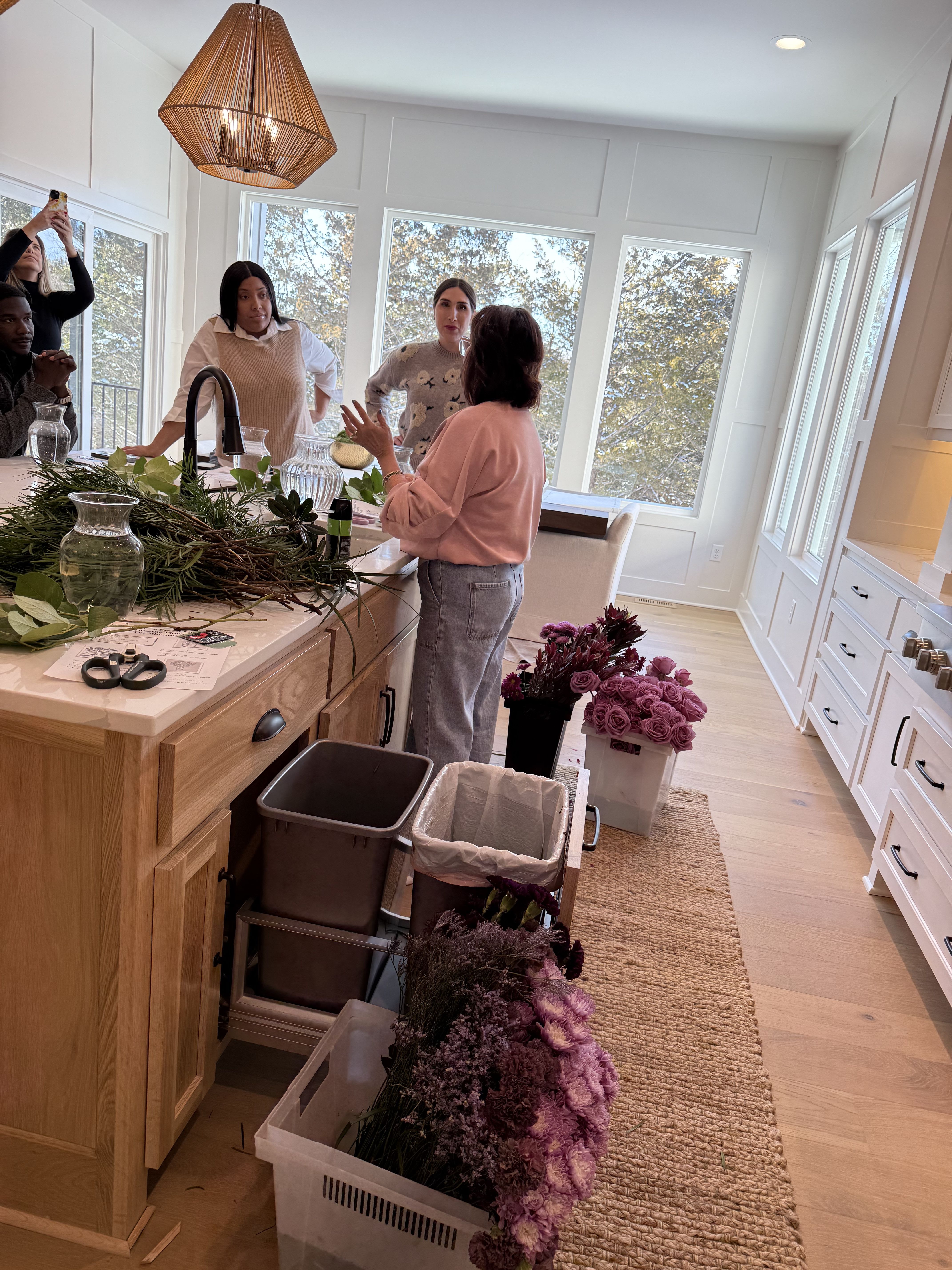 People arranging purple flowers and greenery on a kitchen island