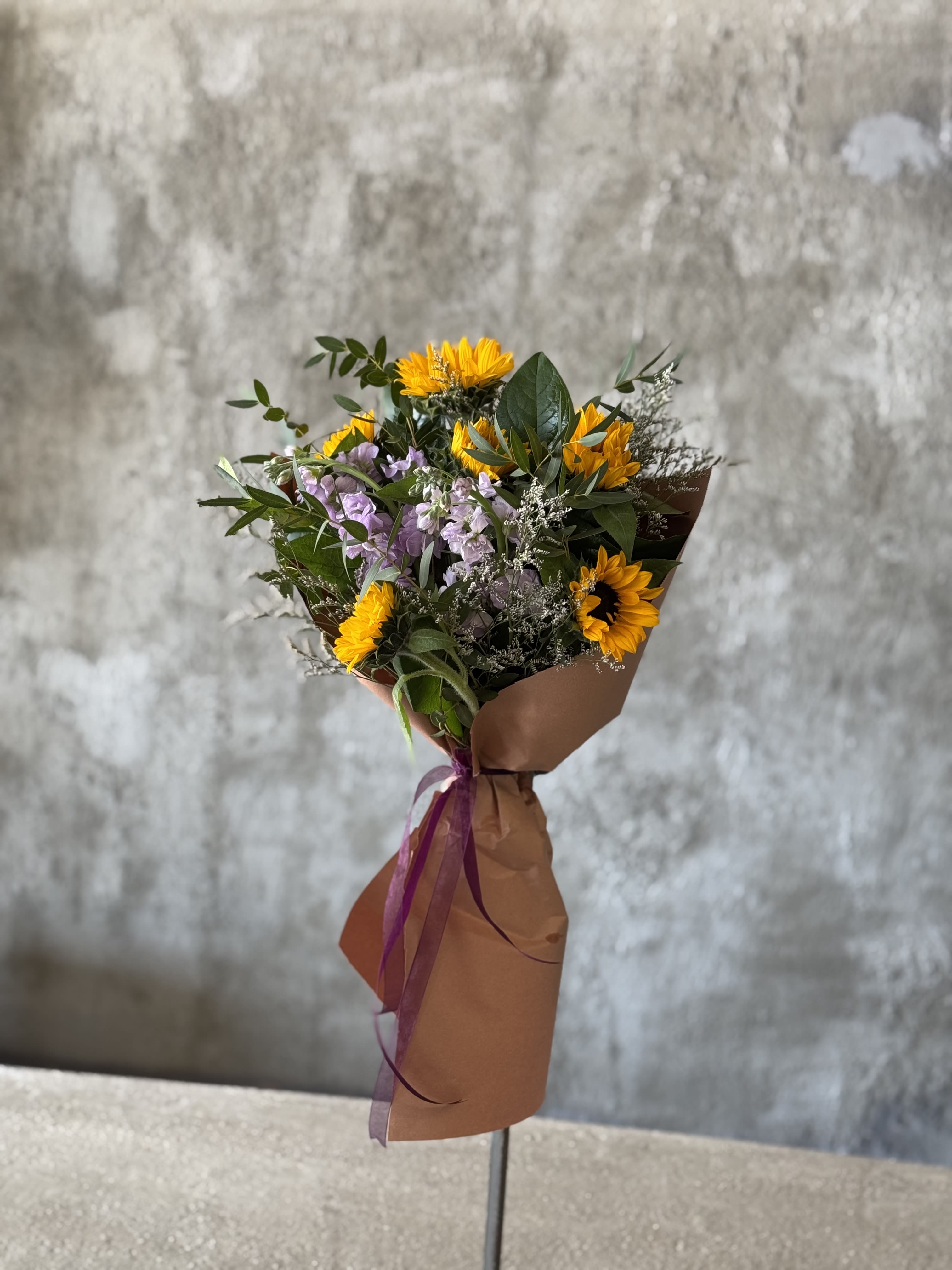 Bouquet of yellow sunflowers and lavender flowers wrapped in brown paper