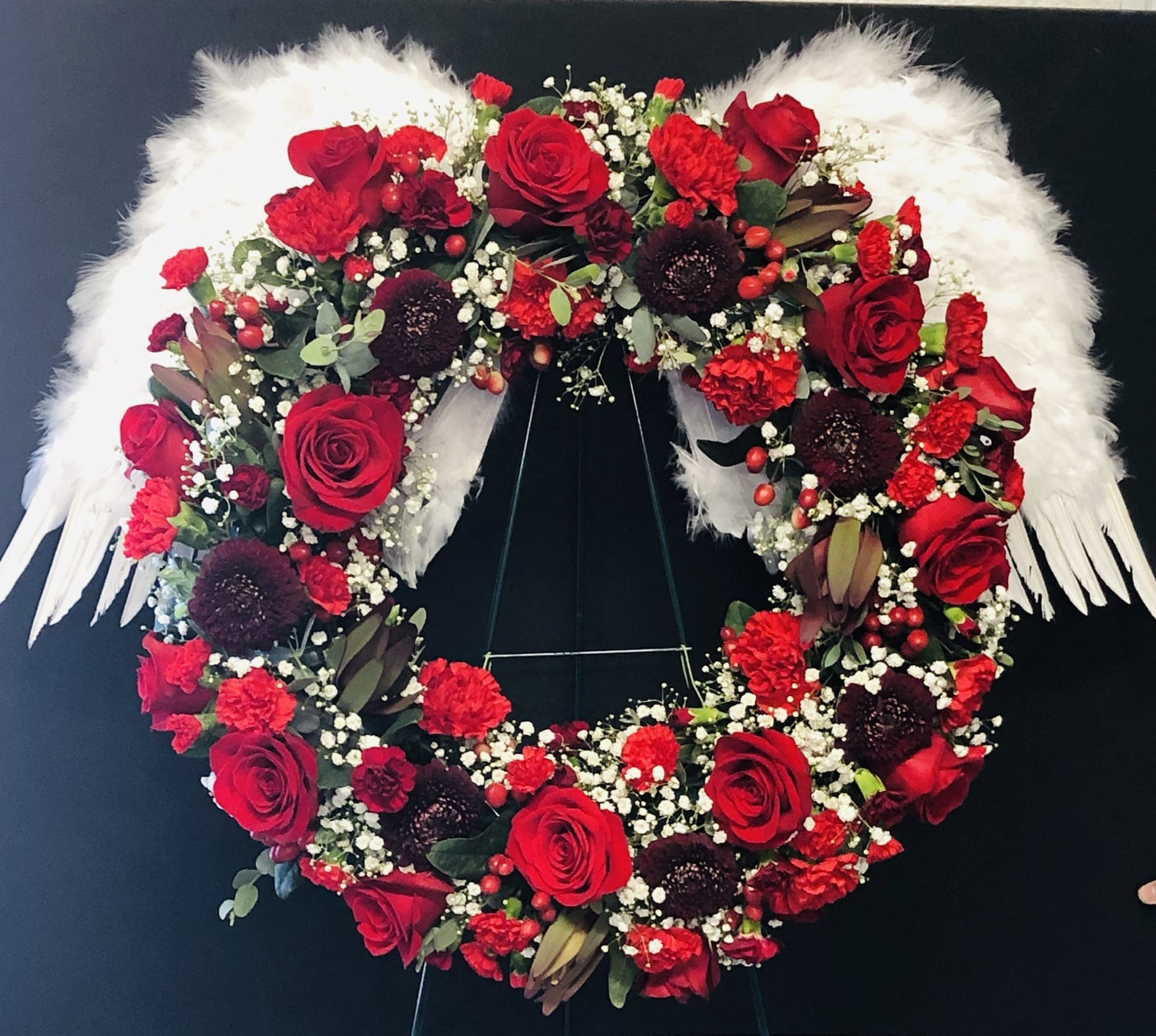 Heart-shaped floral wreath with red roses and white feathers