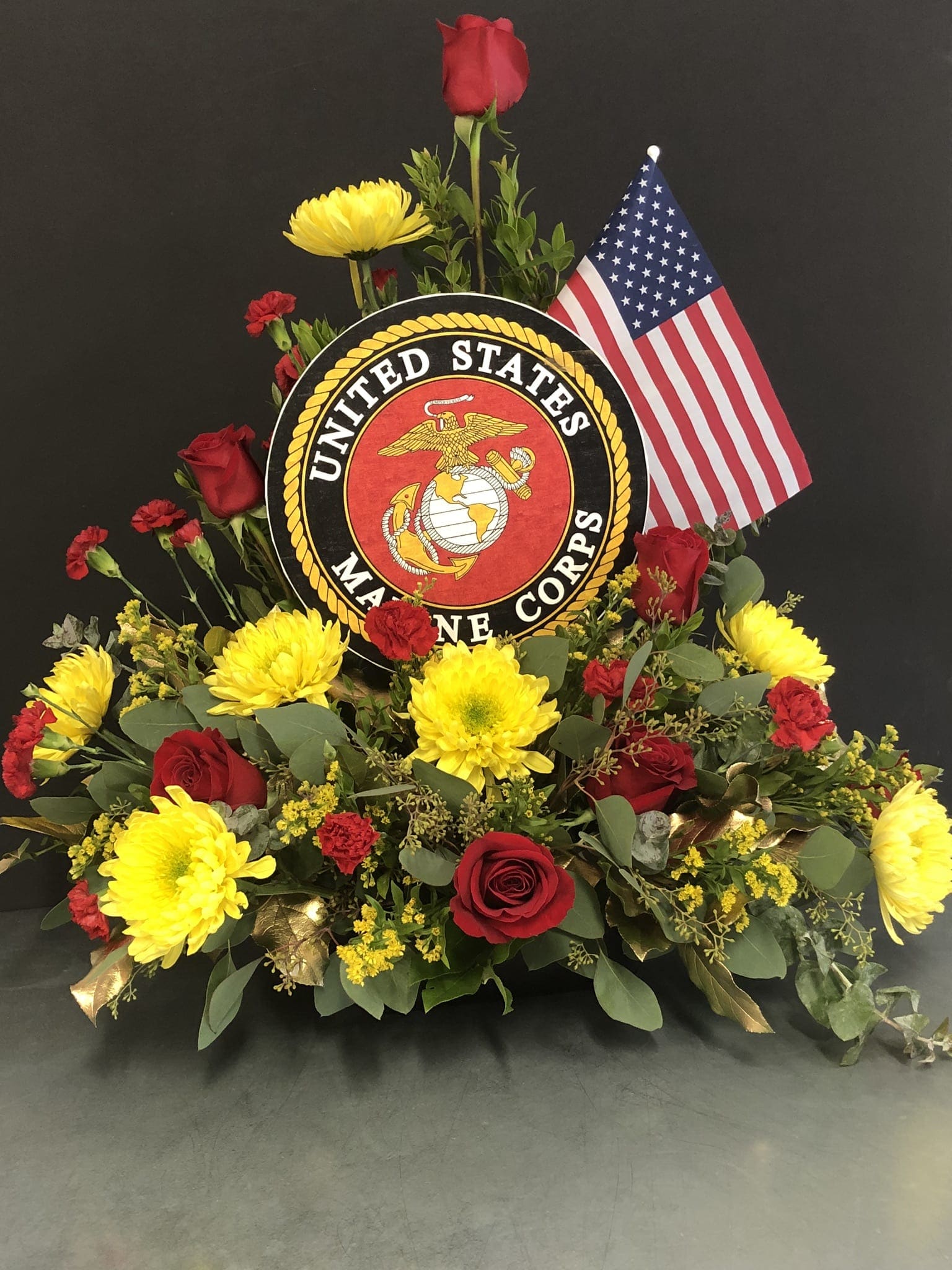 Floral tribute with red roses, yellow mums, and a U.S. Marine Corps emblem