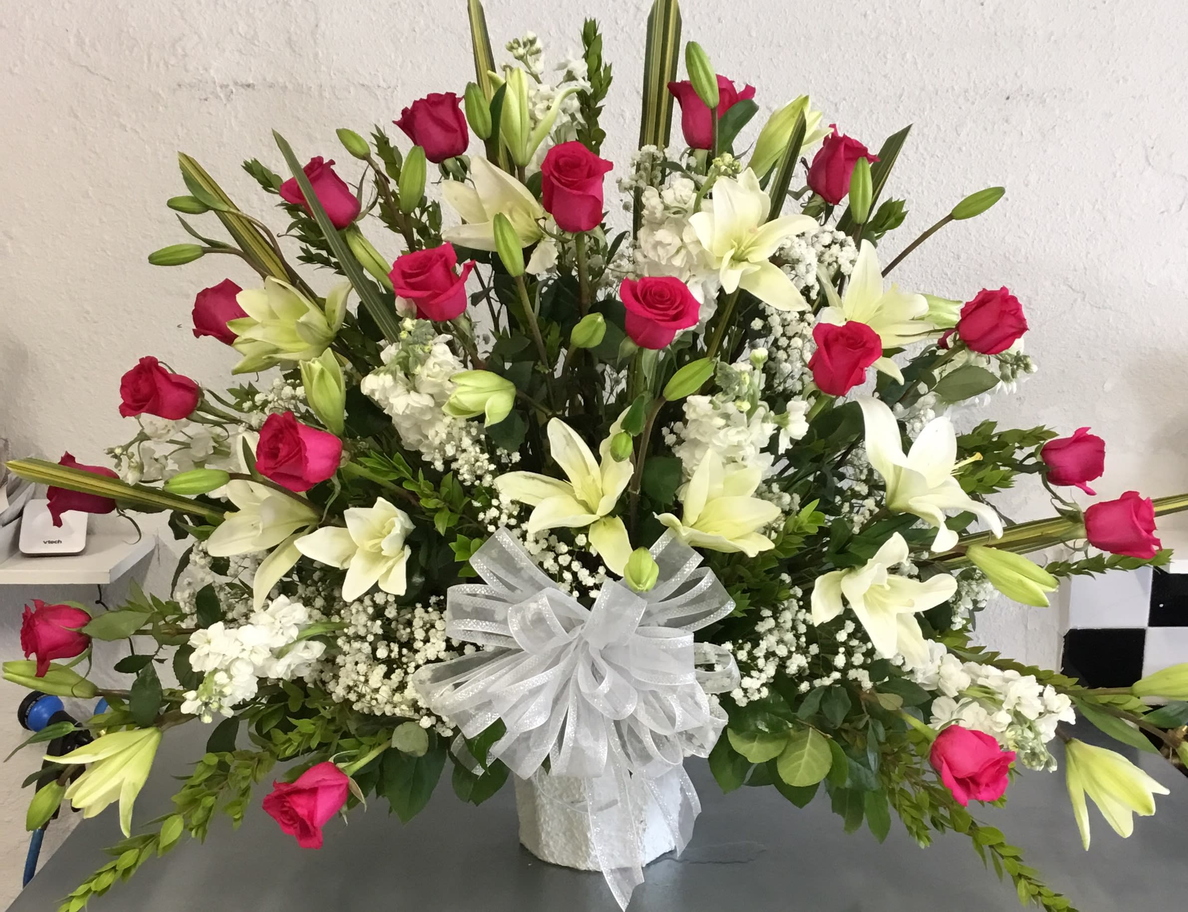 Large bouquet of pink roses and white lilies in a white vase with a sheer bow