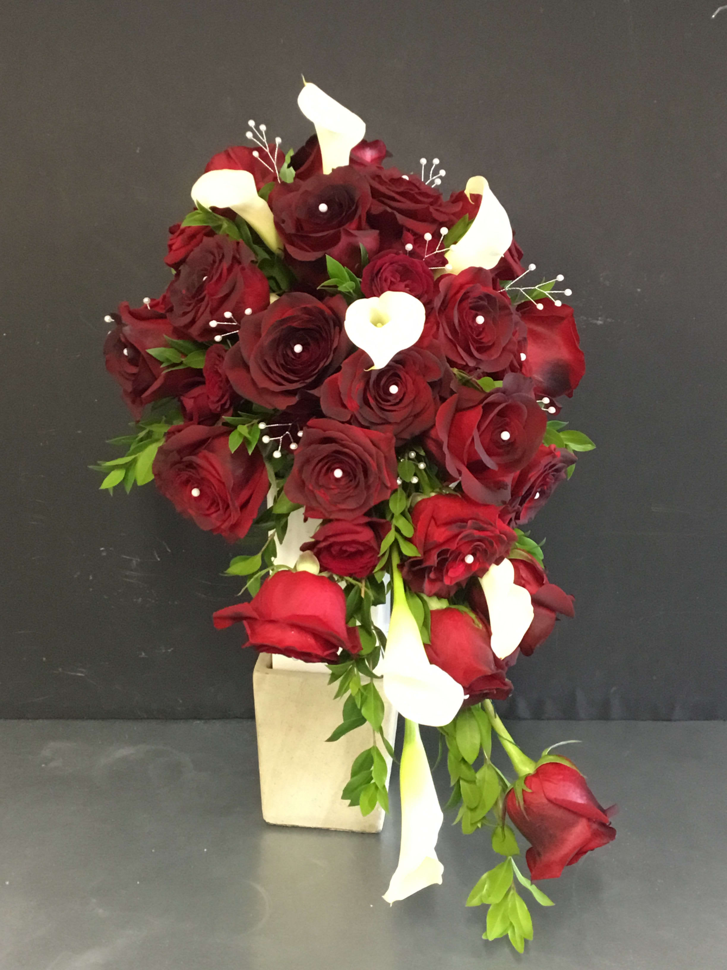 Cascade bouquet of red roses and white calla lilies in a beige vase