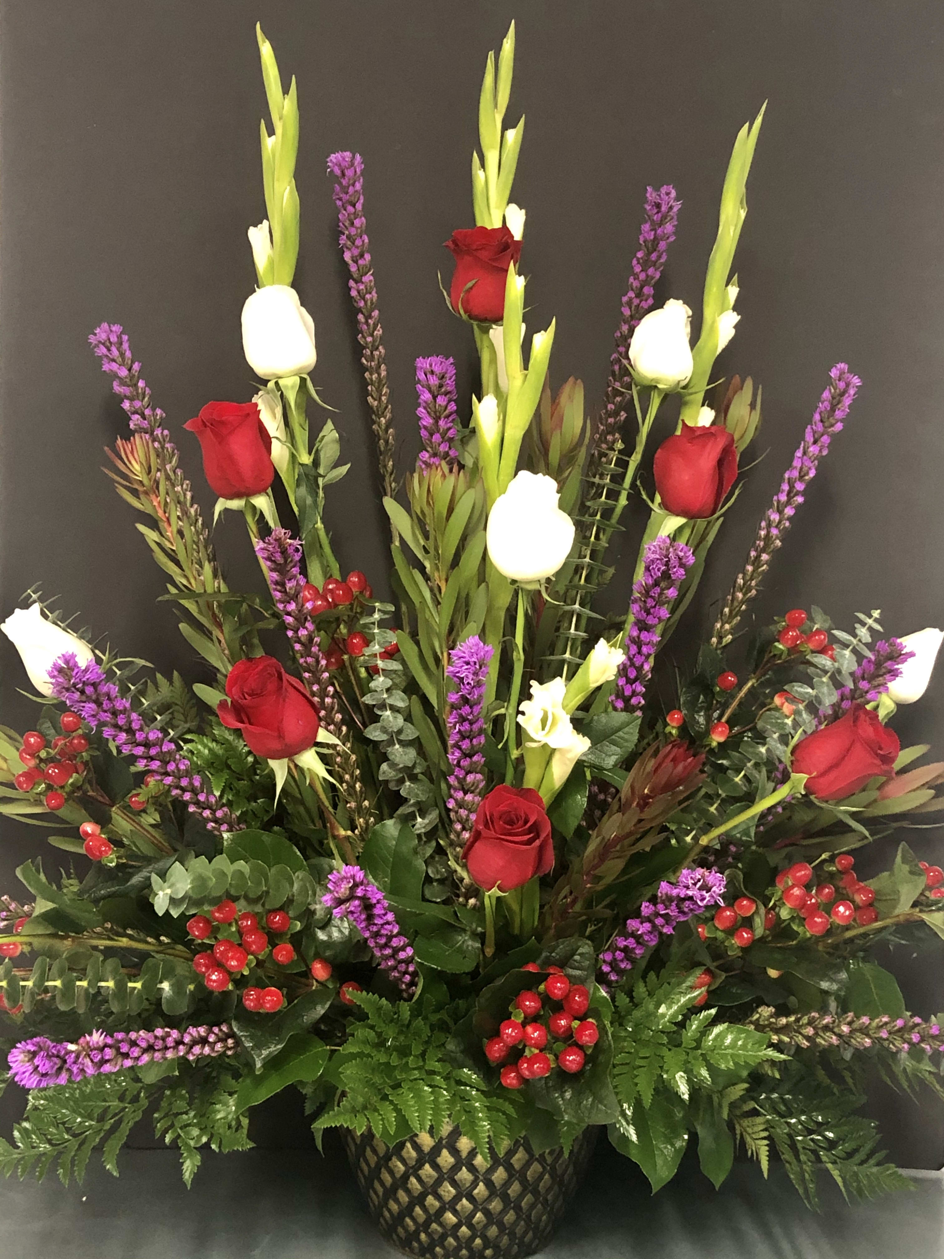 Tall arrangement of red and white roses with purple spikes in a decorative vase