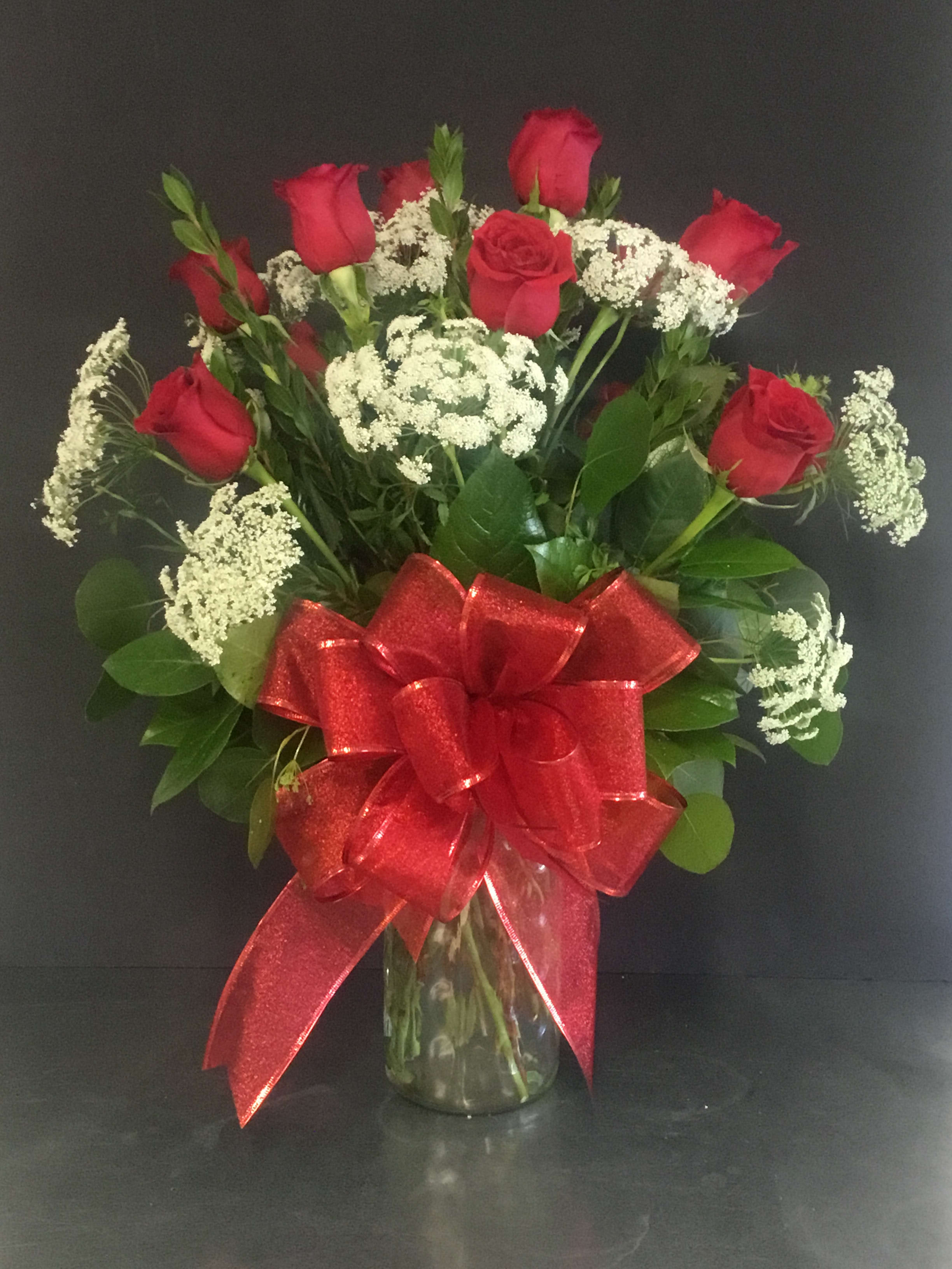 Tall arrangement of red roses and white filler flowers in a clear glass vase with a large red bow.