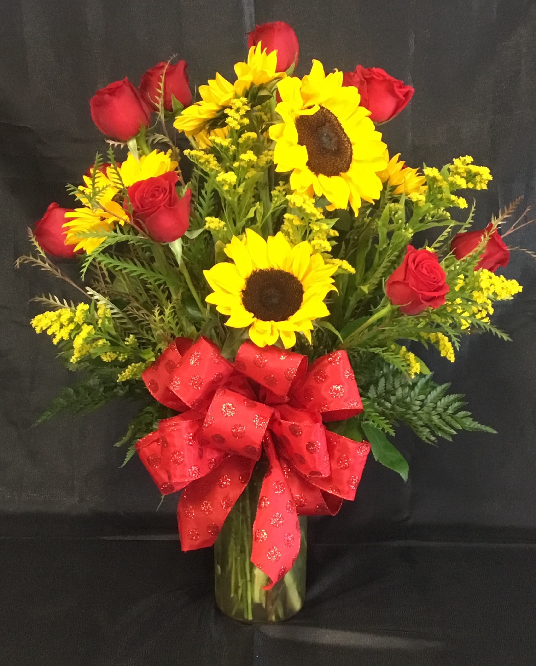 Bouquet of red roses and yellow sunflowers in a glass vase with a red bow