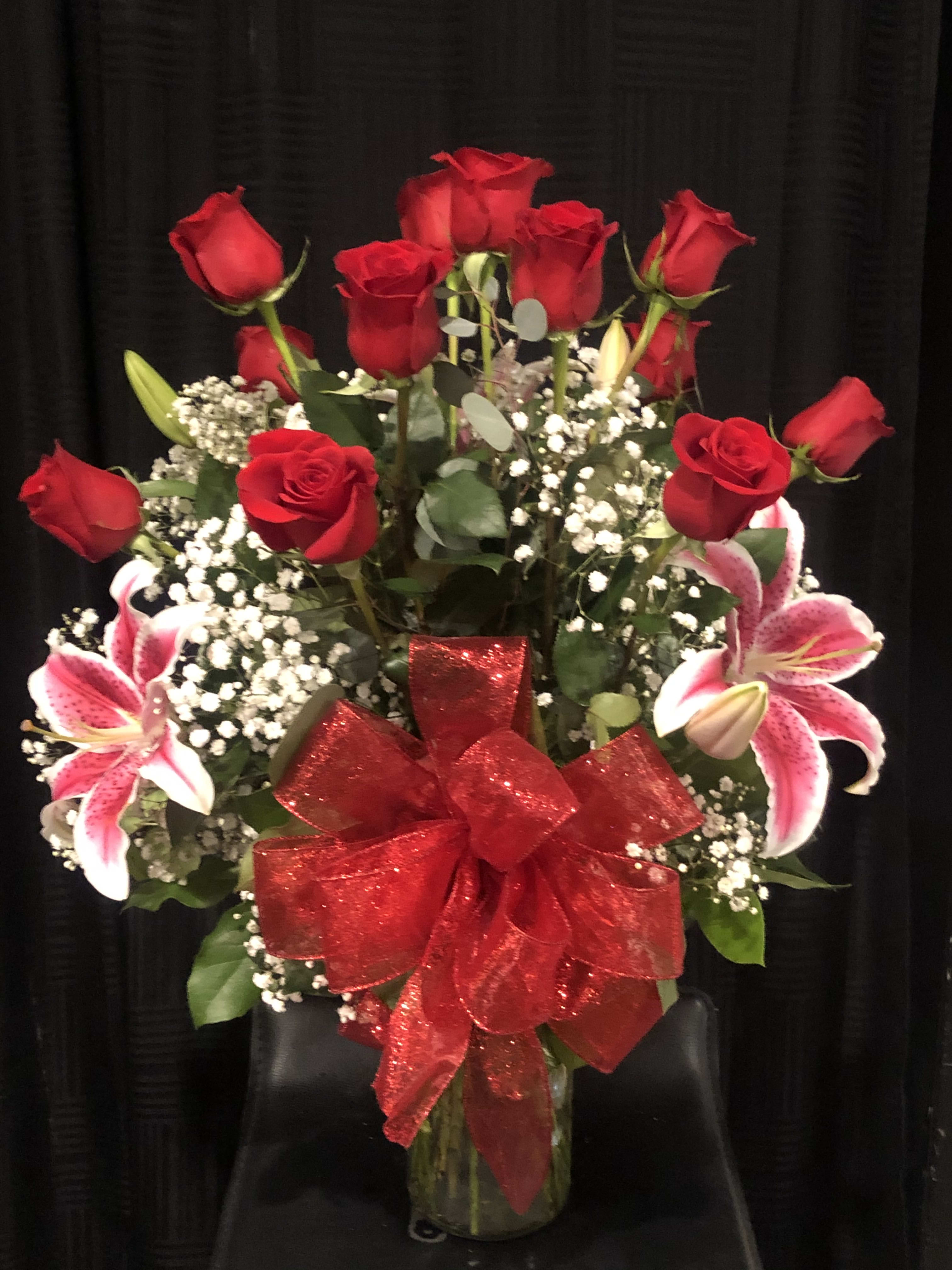 Red roses and pink lilies arranged in a glass vase with a red bow.