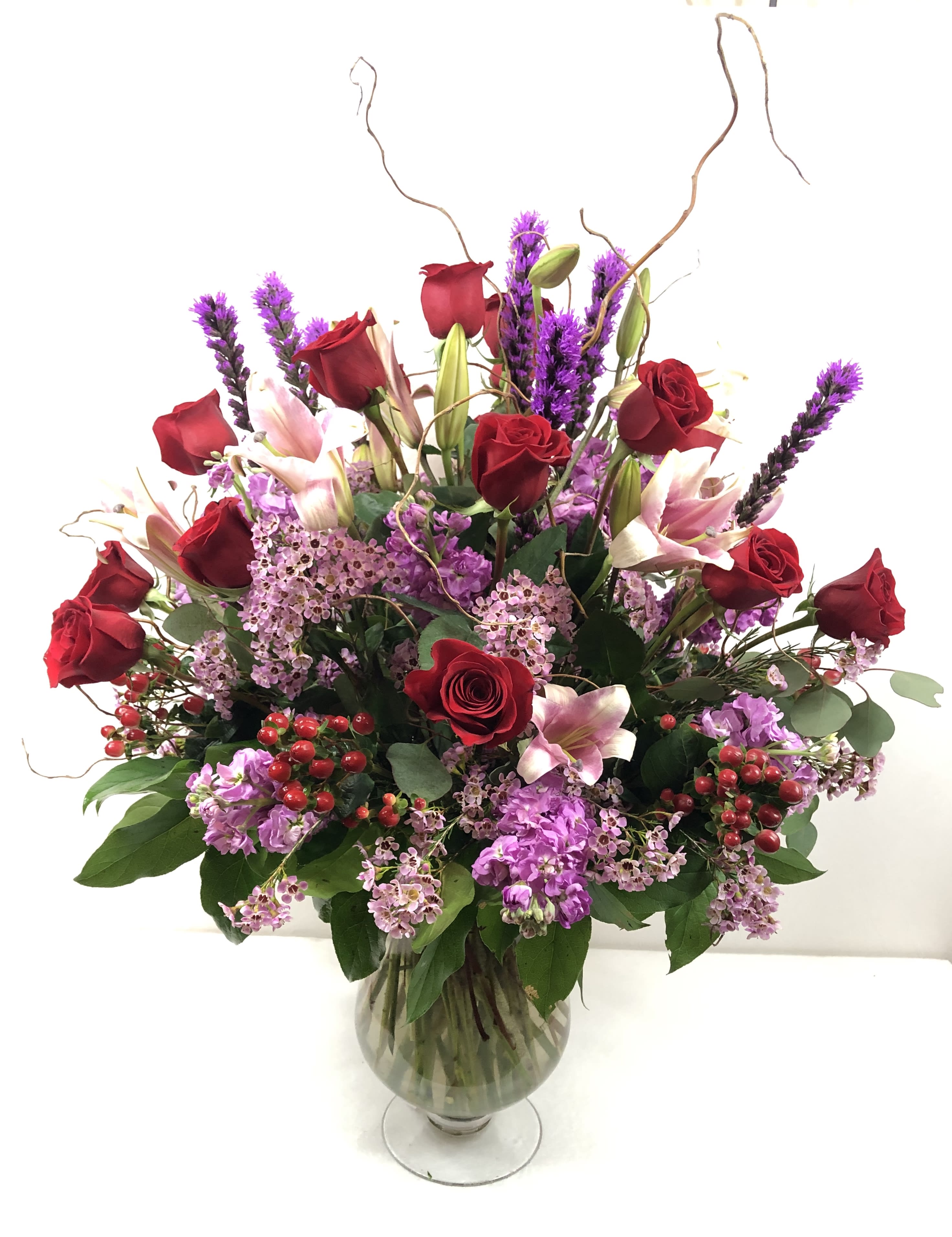 Red roses and pink lilies in a glass vase with purple filler flowers