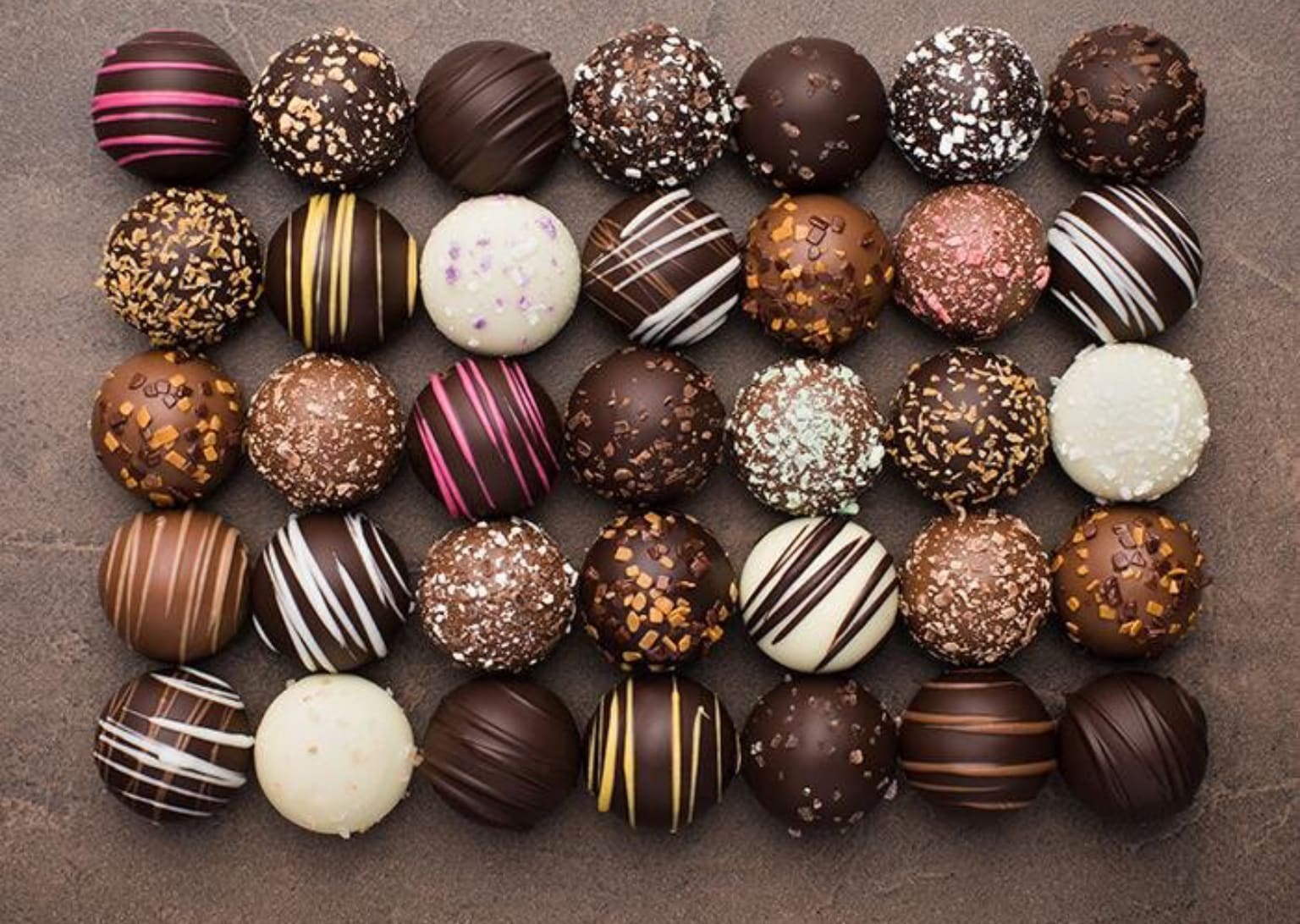 Assorted chocolate truffles arranged in rows on a flat surface