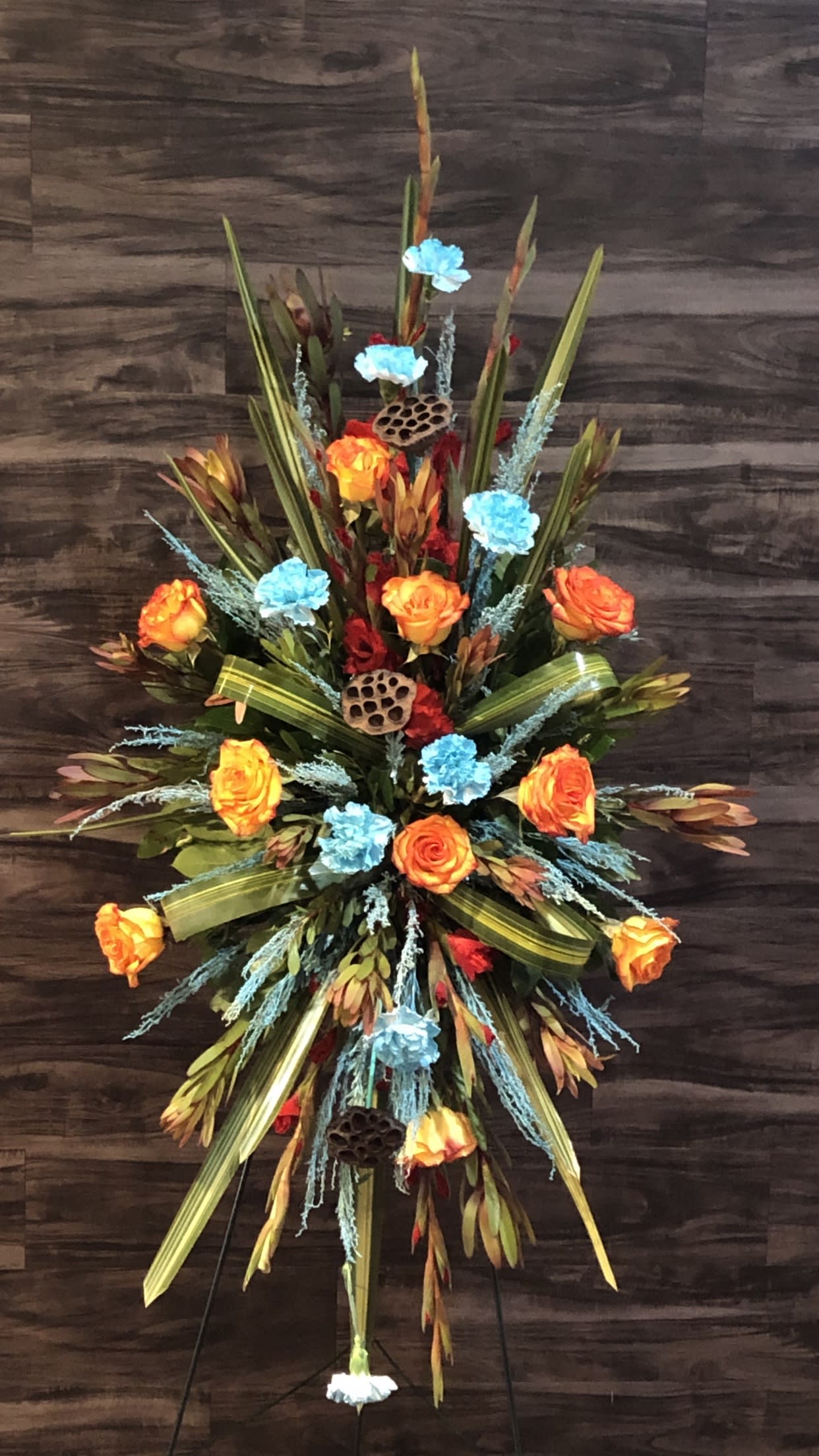 Tall floral spray with orange roses and blue accents on a stand