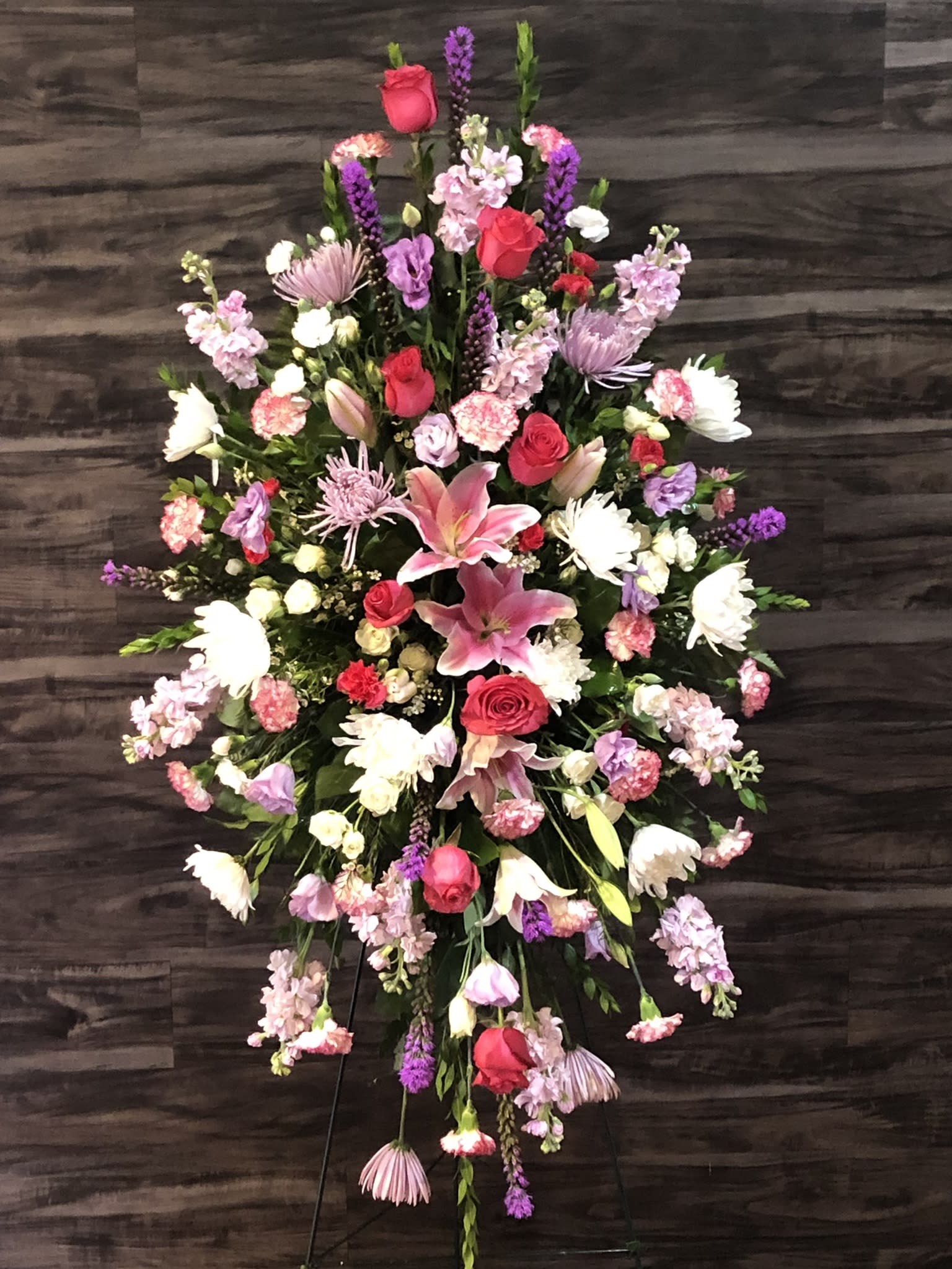 Large standing floral spray with pink lilies, red roses, and purple blooms