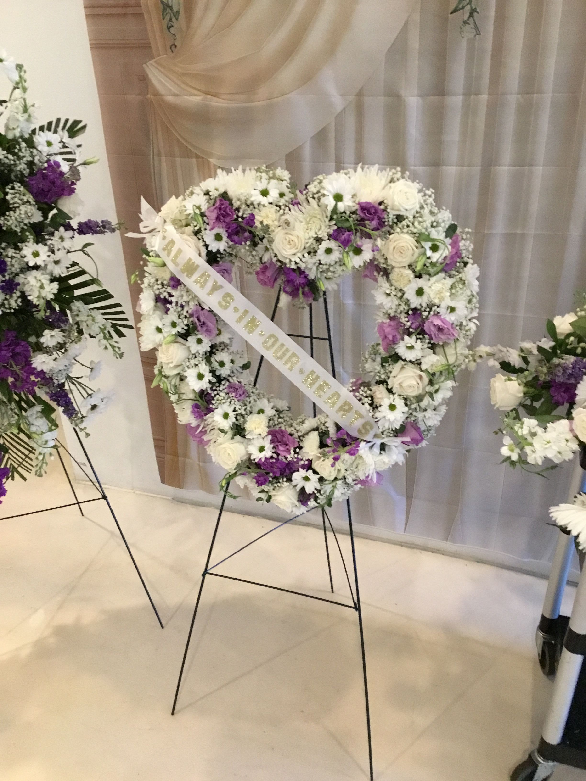 Heart-shaped floral wreath on a stand with white and purple flowers