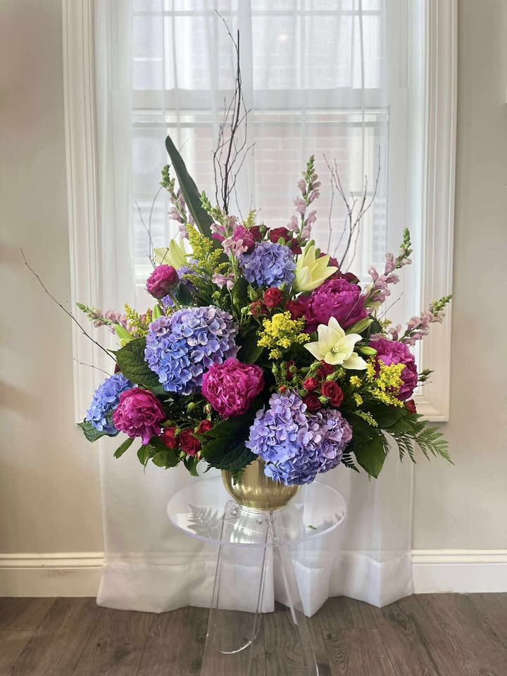 Large floral arrangement in a gold vase with blue, pink, and white blooms