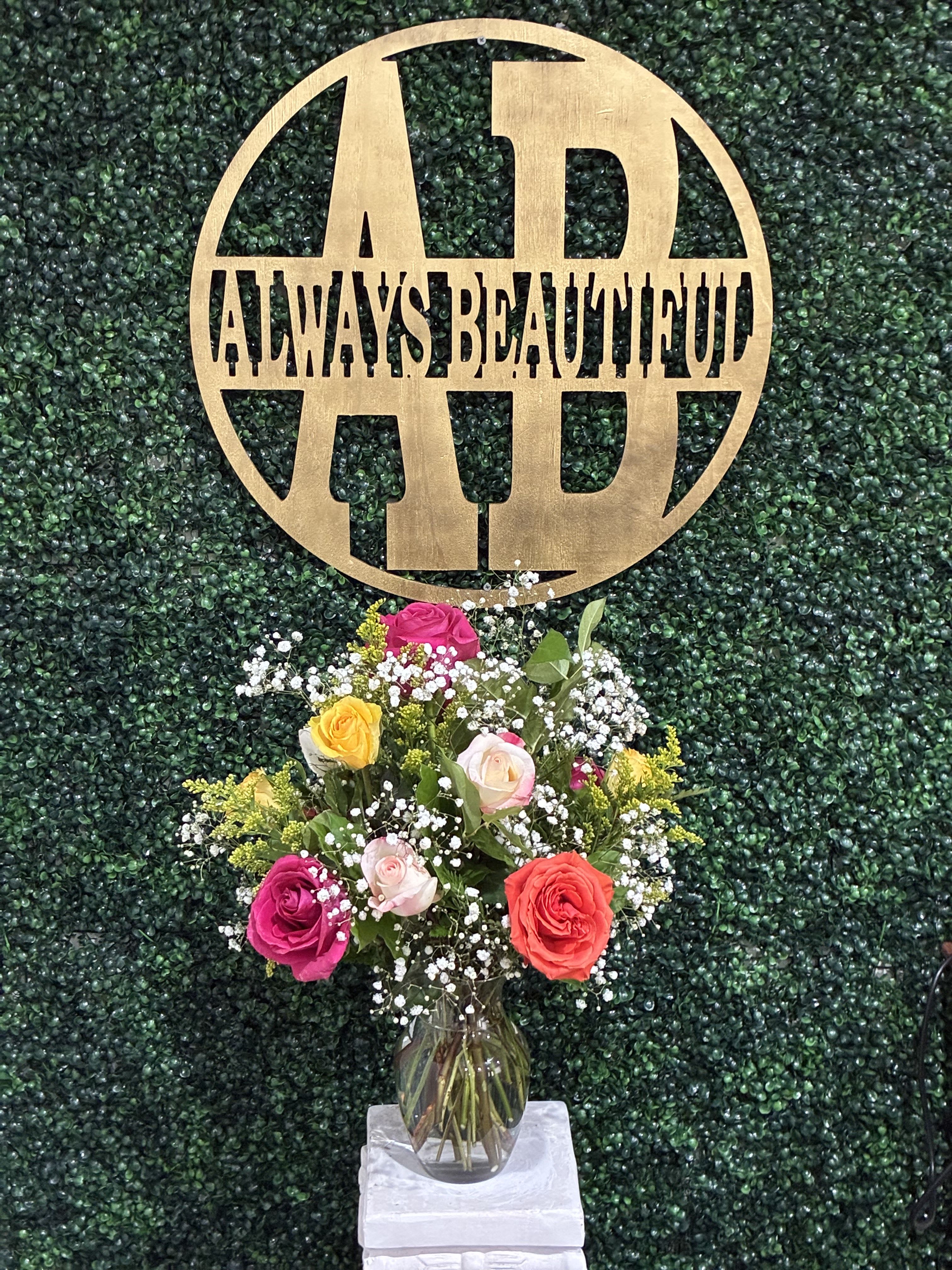 Mixed rose bouquet in a glass vase beneath a gold monogram sign